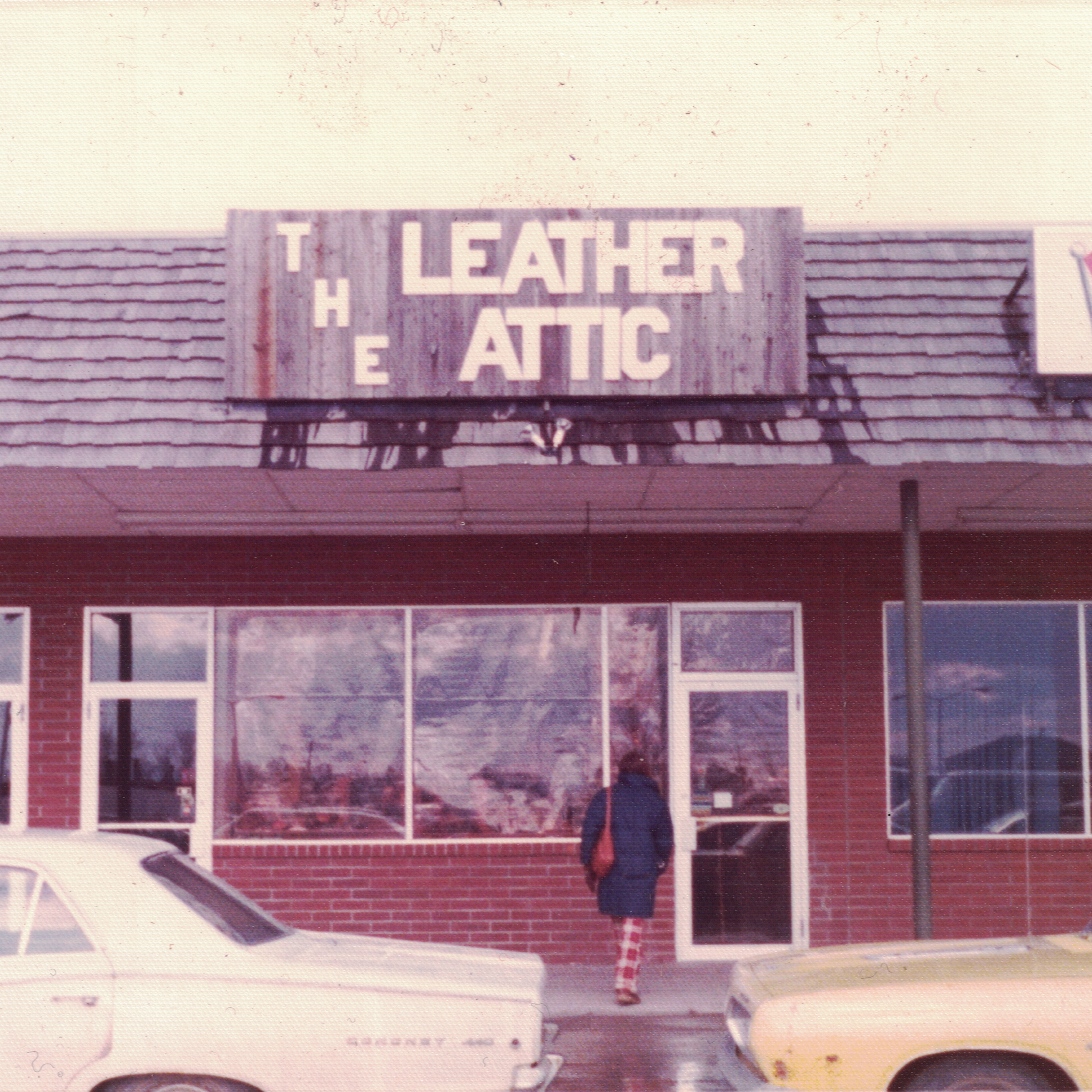 A rooftop sign with the words 'LEATHER' and 'ATTIC' on it, likely part of a larger sign, with part of a person standing below in the foreground.
