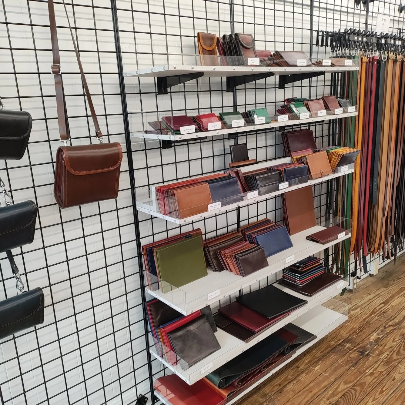 Display of leather wallets, purses, and belts on metal and white shelves at a store.