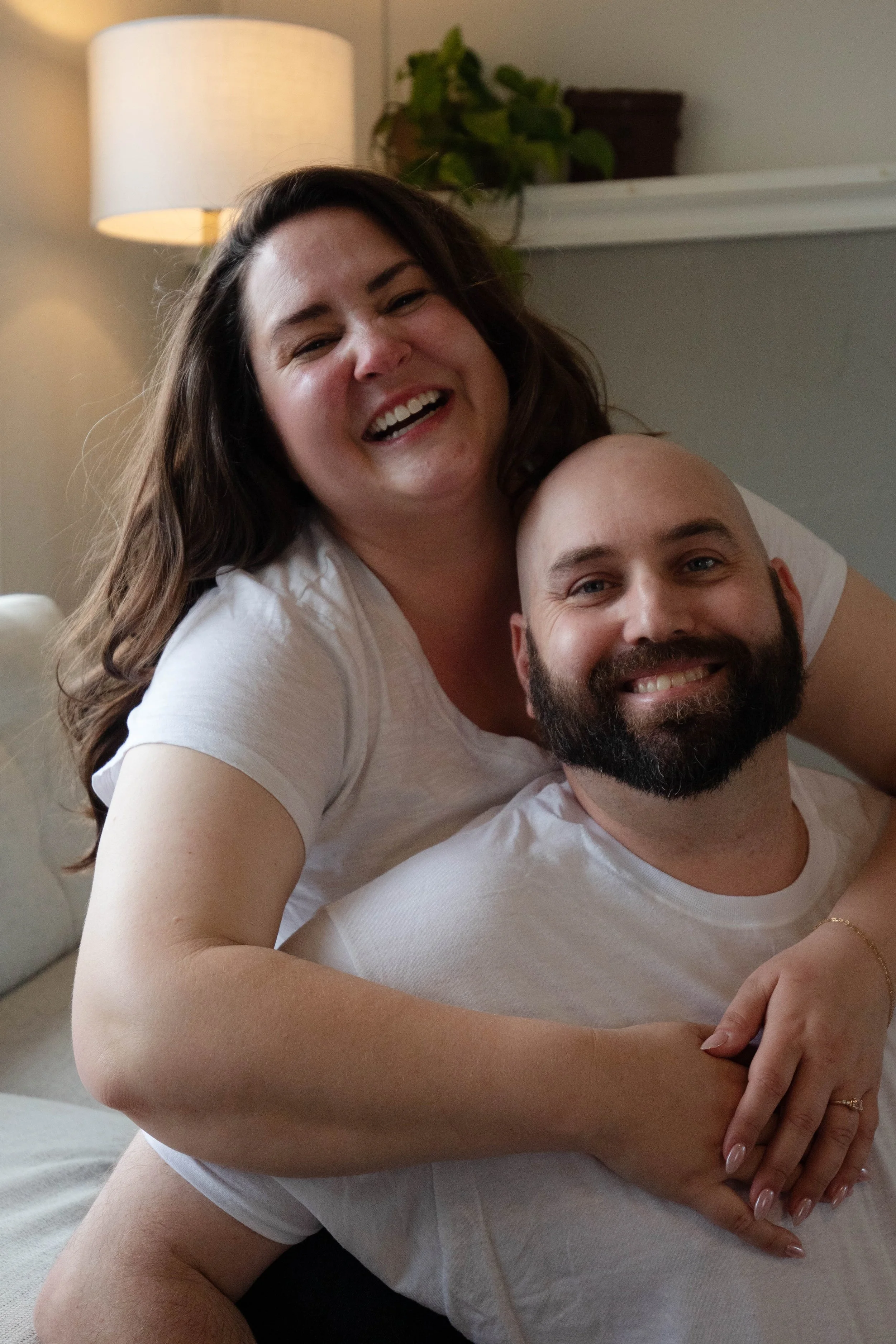 A happy woman and a man smiling together, with the woman resting on the man’s shoulders in a cozy living room setting.