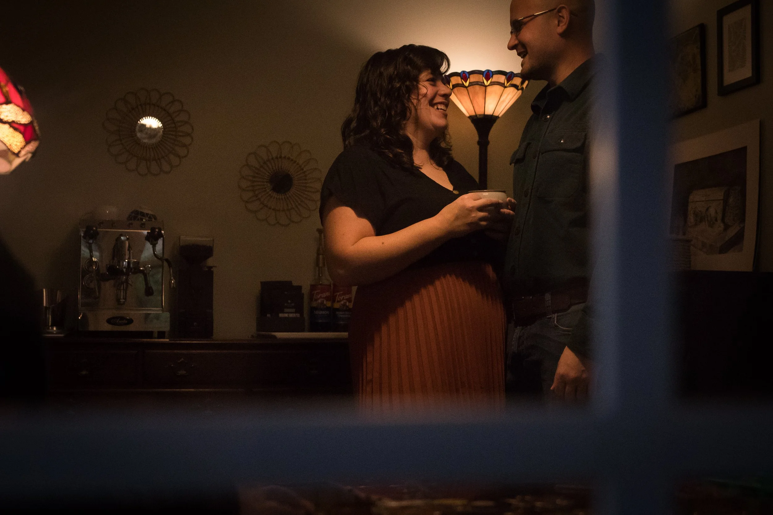 A woman and a man smiling and talking at a social gathering in a dimly lit room, with warm lighting and decorative wall art.