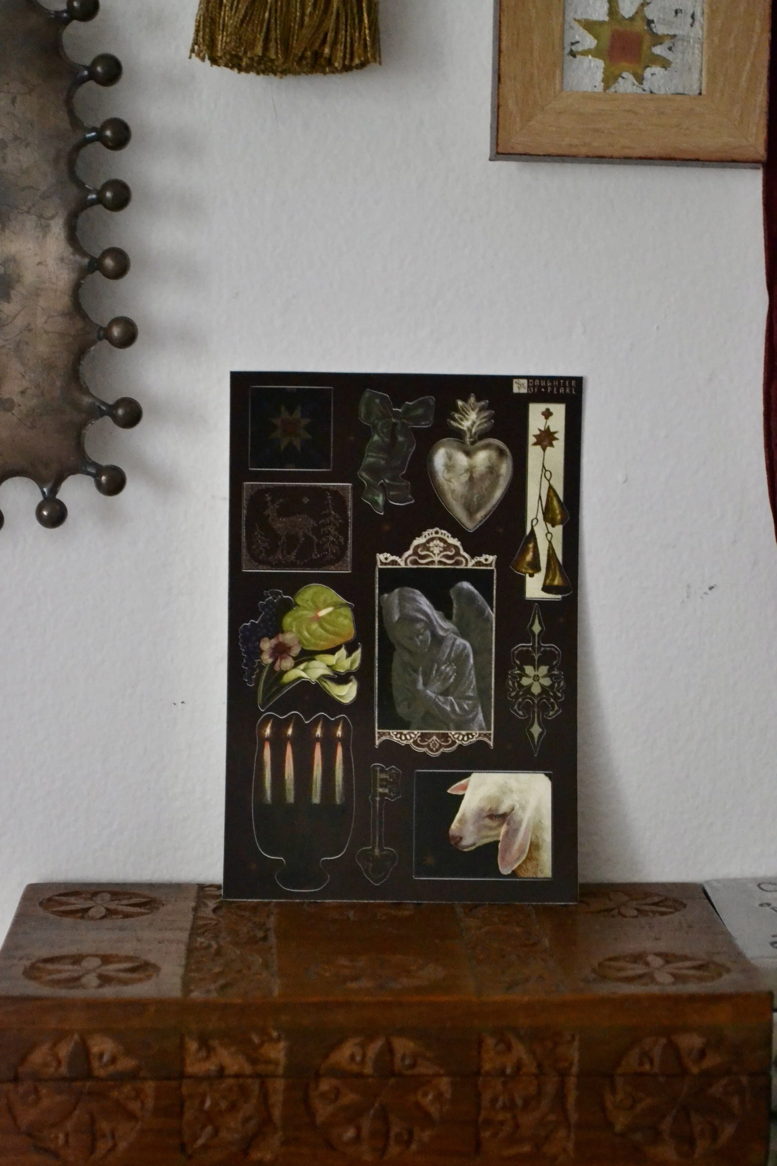 A sticker sheet with various images, including a candle holder with lit candles, a stone angel, a sacred heart, and a goat.