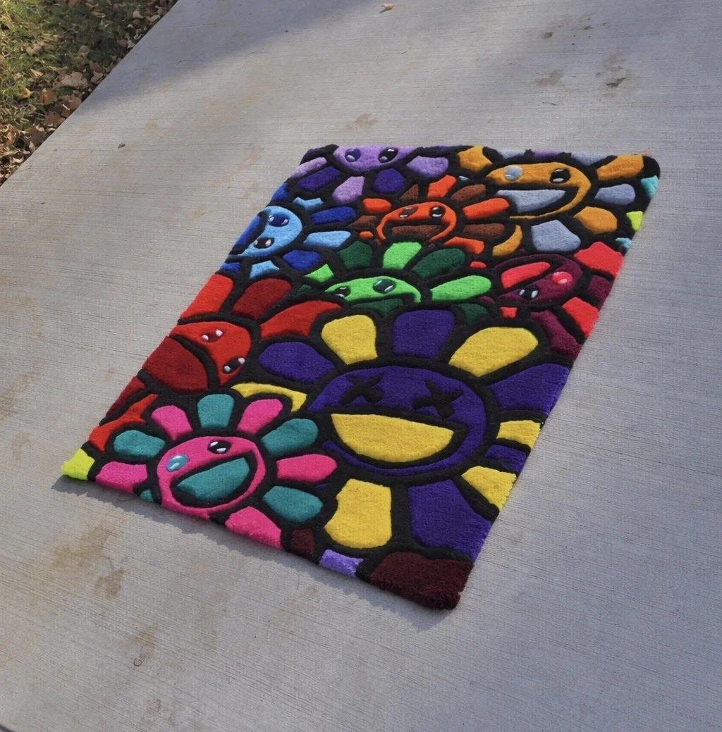 Colorful, plush rug with cartoon-style smiling sun faces in various bright colors, placed on a concrete surface outdoor.