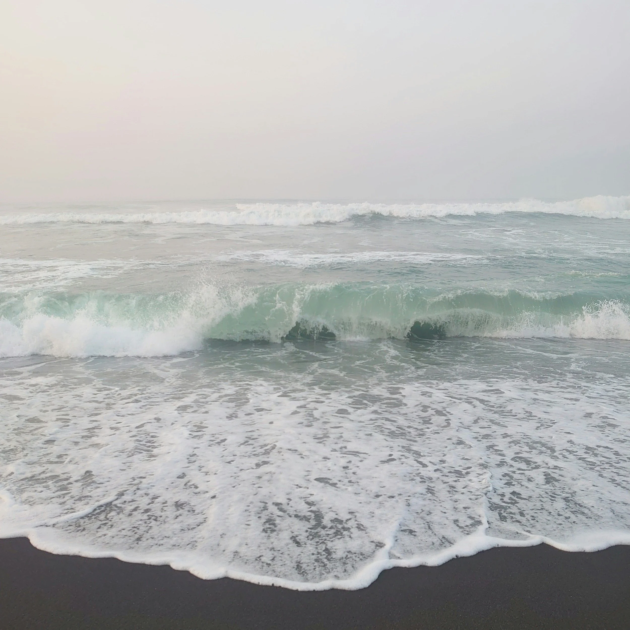 Ocean waves crashing onto a sandy beach with overcast sky