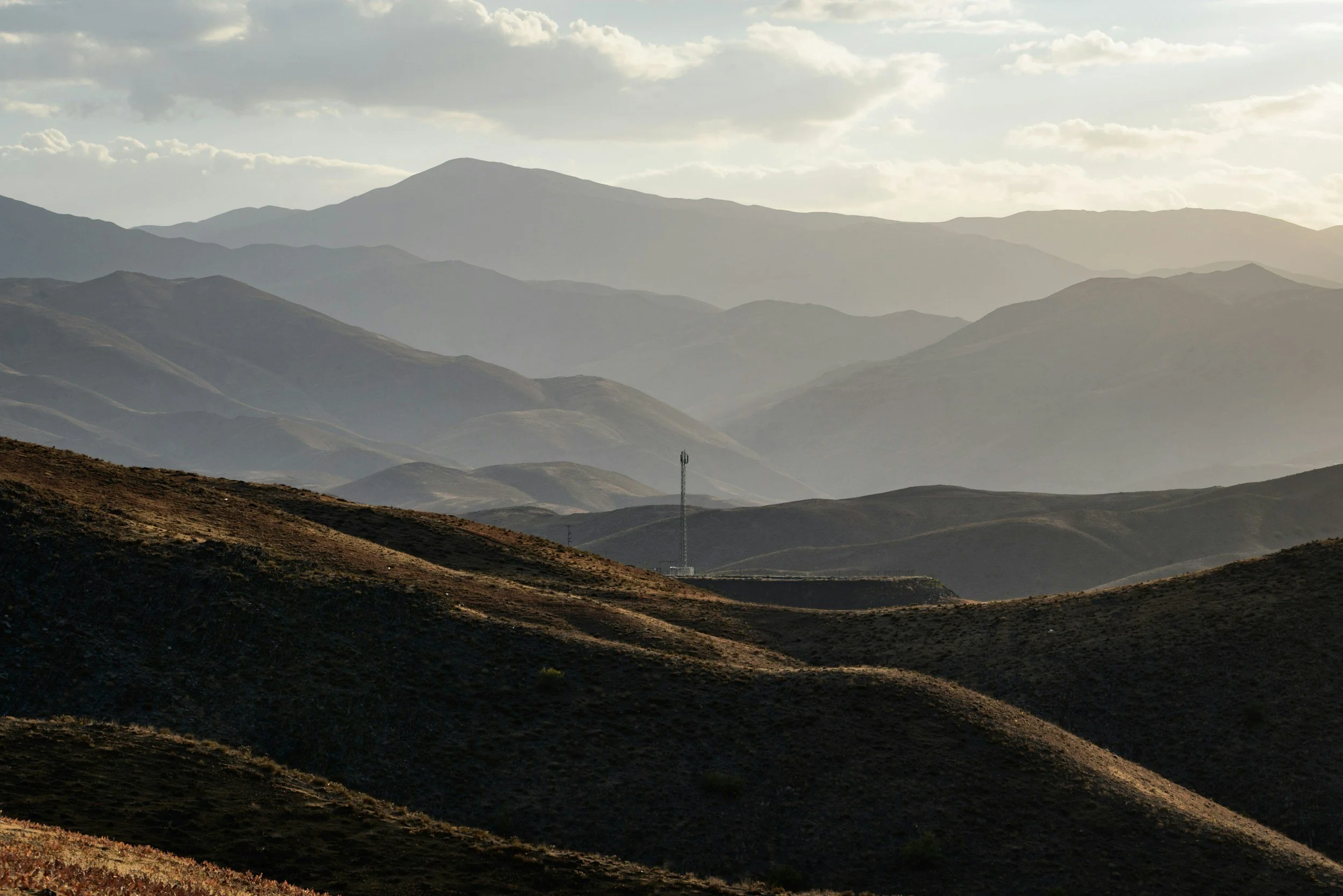 A landscape of rolling mountains with a metallic tower in the middle and a cloudy sky above.