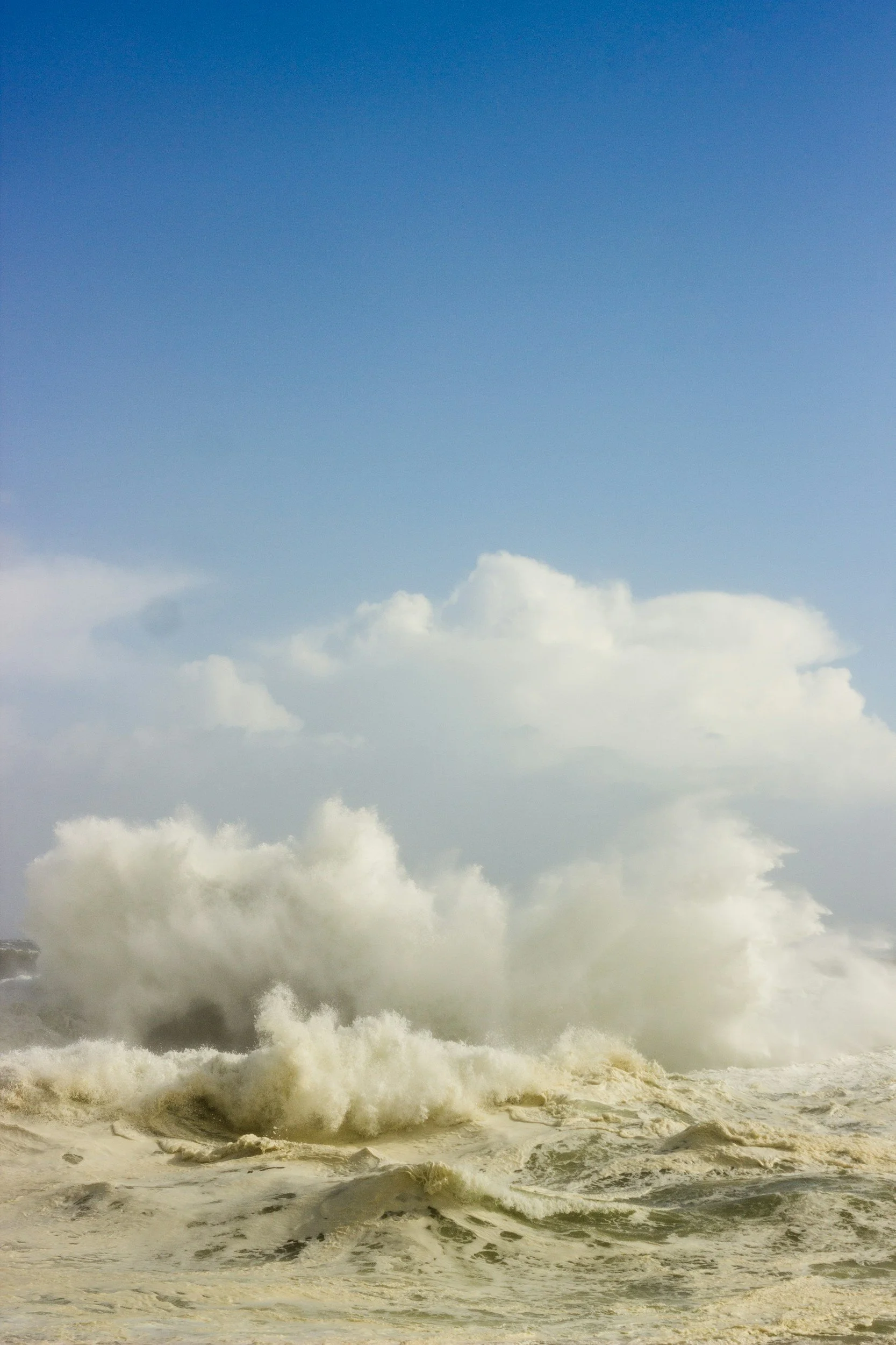 Large ocean waves crashing with white foam under a partly cloudy sky.