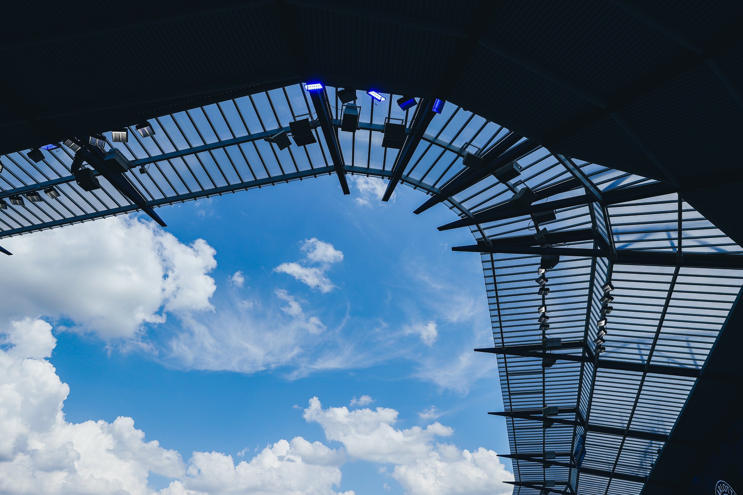 Looking up at a modern building with glass and metal panels against a blue sky with scattered white clouds.
