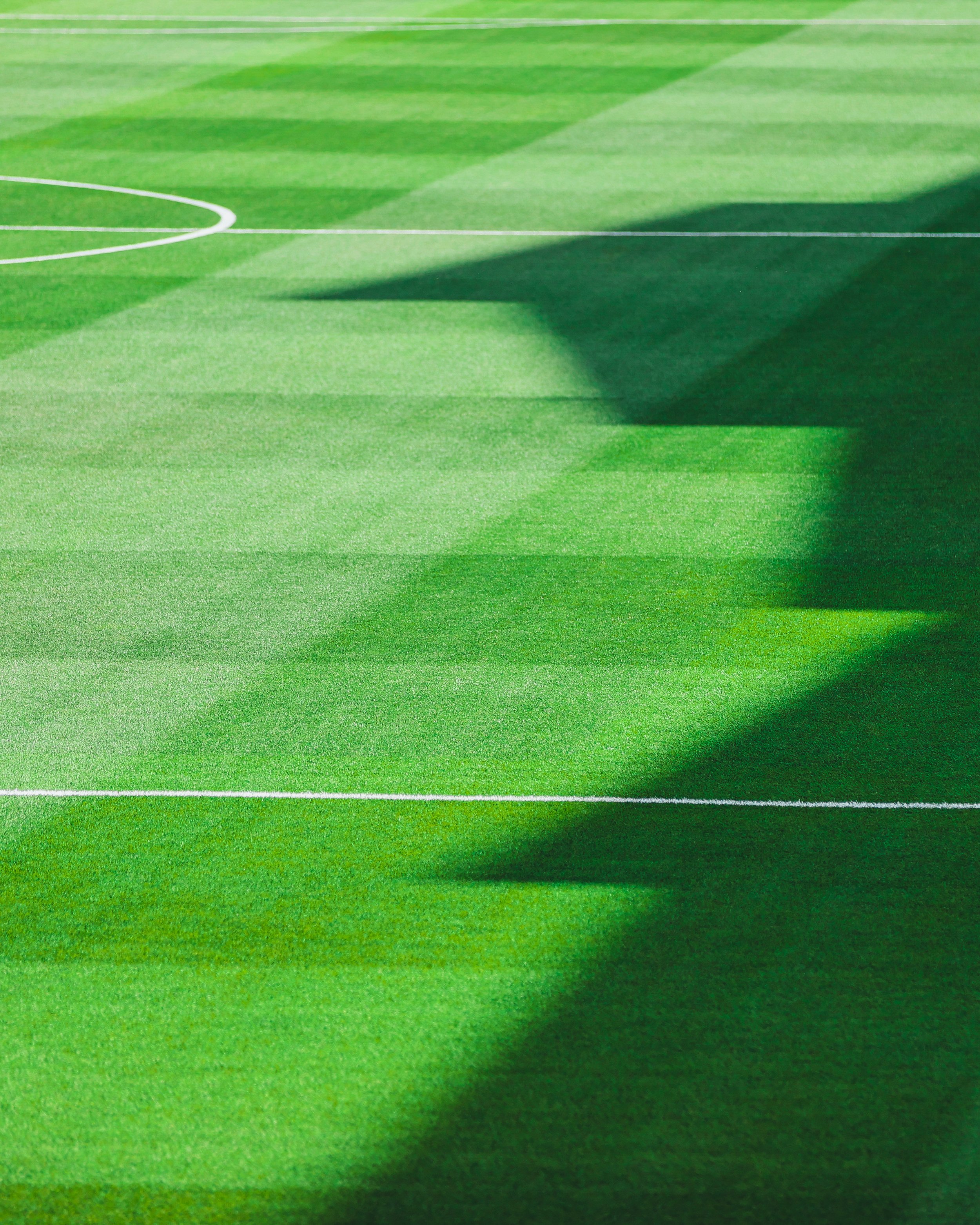 Close-up of a green grass field with white boundary lines, partially shaded.