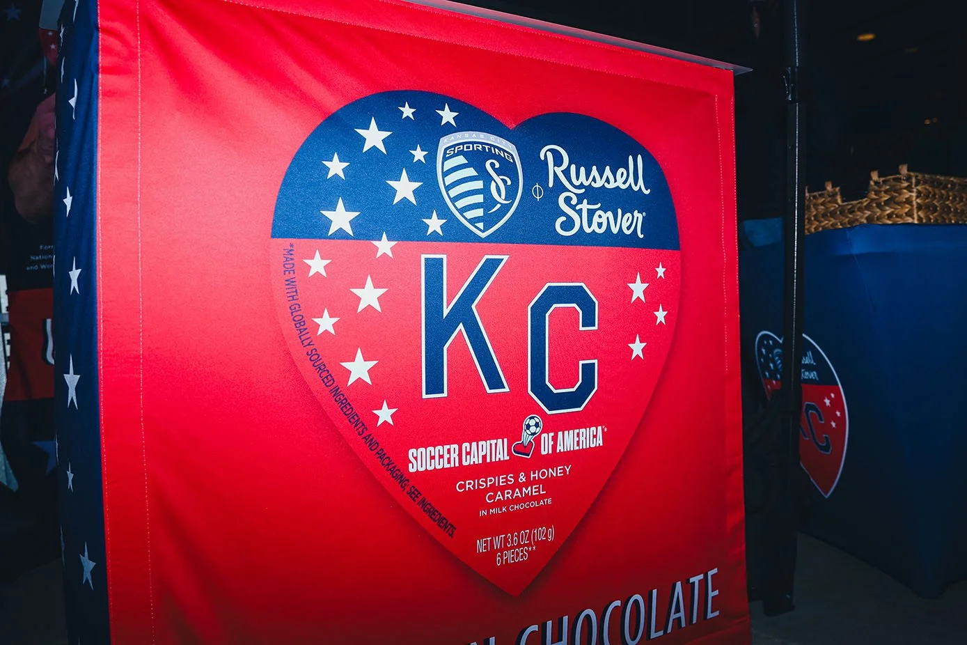 A large red chocolate box with a heart shape design featuring the Kansas City Soccer Team logo and the words 'KC', 'Russell Stover', and 'Soccer Capital of America'. The box advertises 'Crispies & Honey Caramel' chocolates.