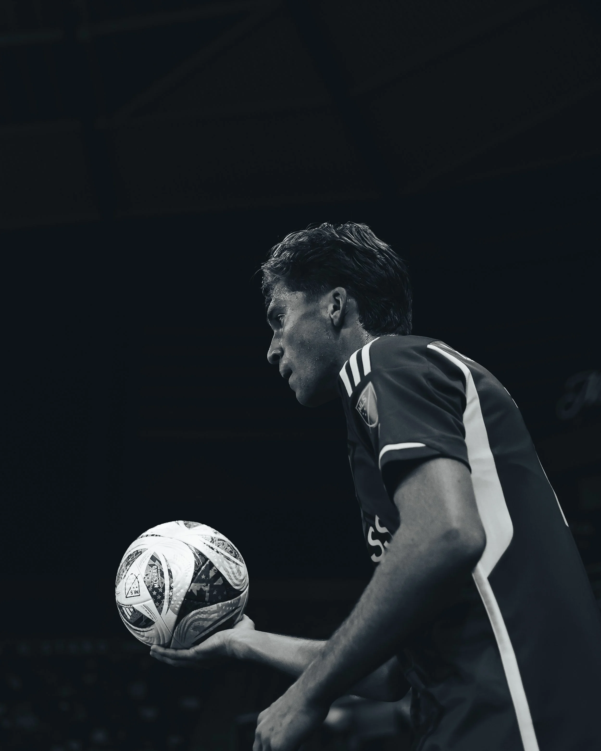 Black and white photo of a man in a sports jersey holding a soccer ball, focusing on his profile as he prepares for a game or practice.