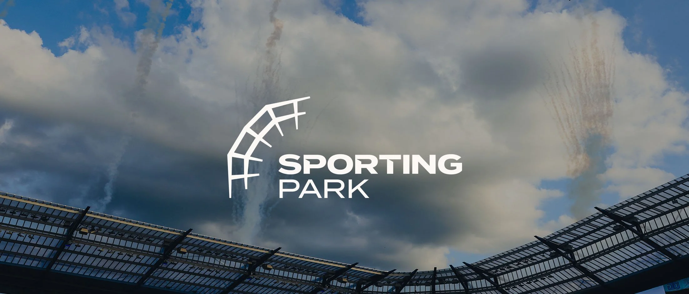 View of an outdoor stadium with a curved seating area at the bottom, under a cloudy sky, displaying the logo of Sporting Park.