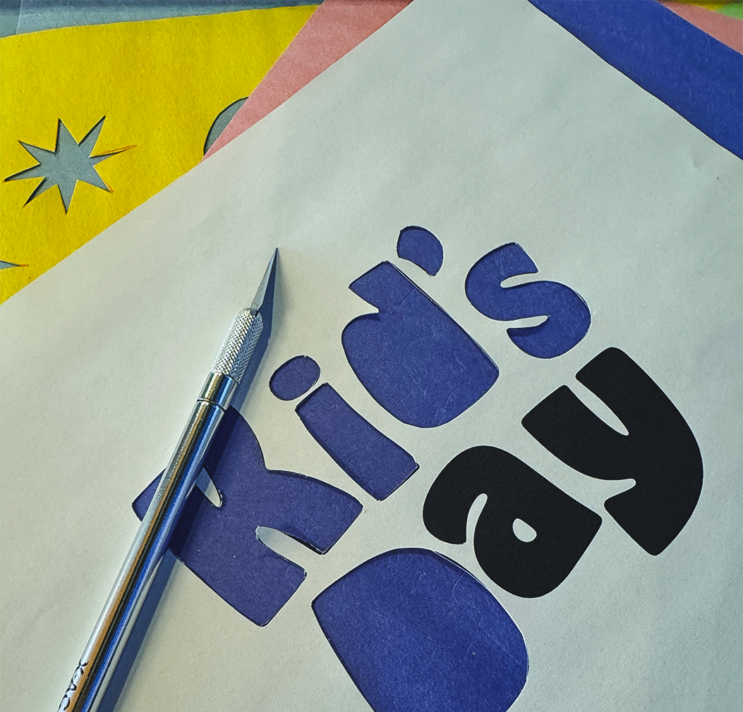 Colorful paper cutout letters spelling 'Happy Birthday' with a craft knife on a white background.