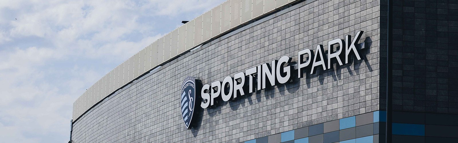 Exterior of a building with the sign 'SPORTING PARK' and a sports team's emblem on the facade.