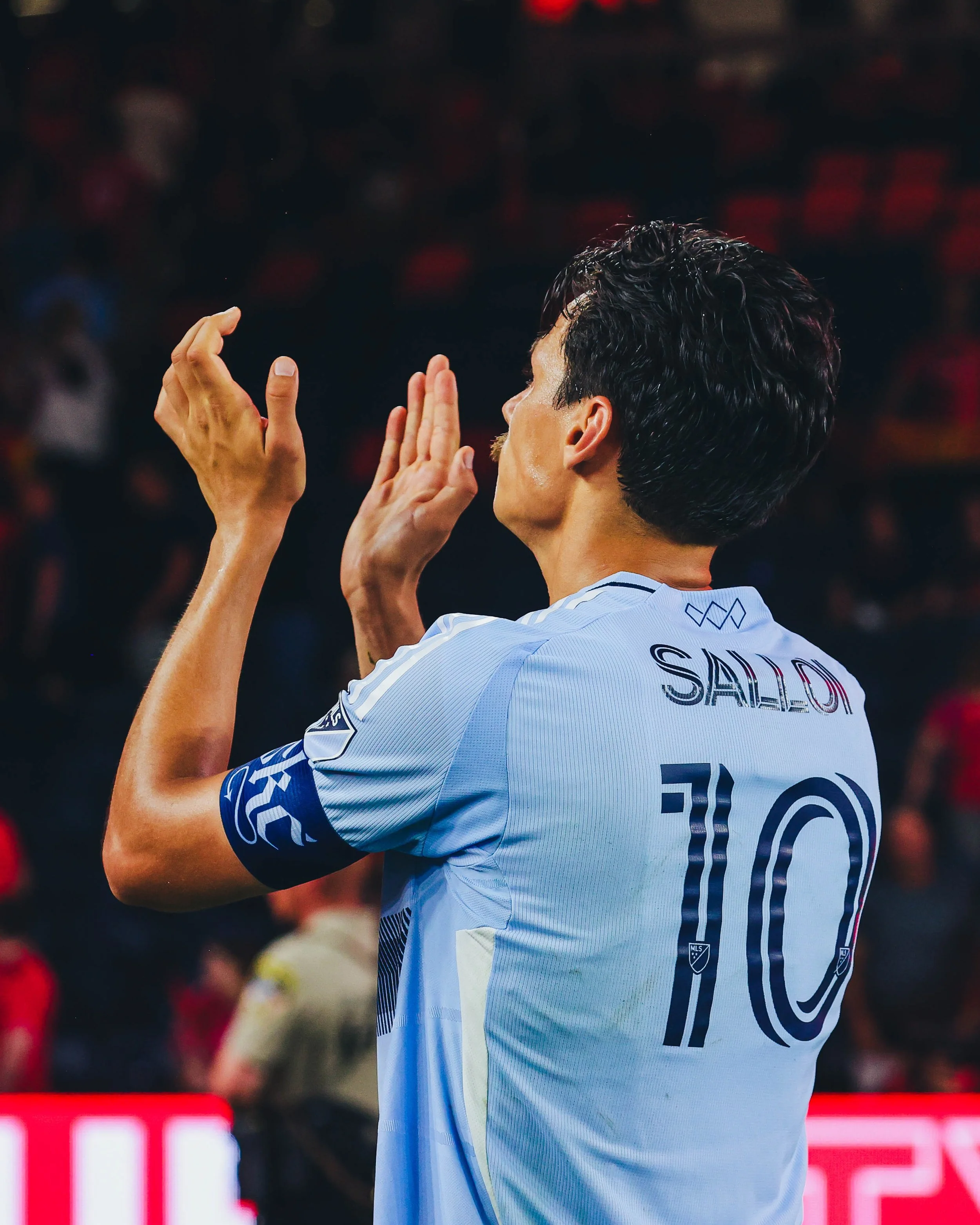 A soccer player in a light blue jersey with the number 10 on the back, standing on a field in front of a crowd.