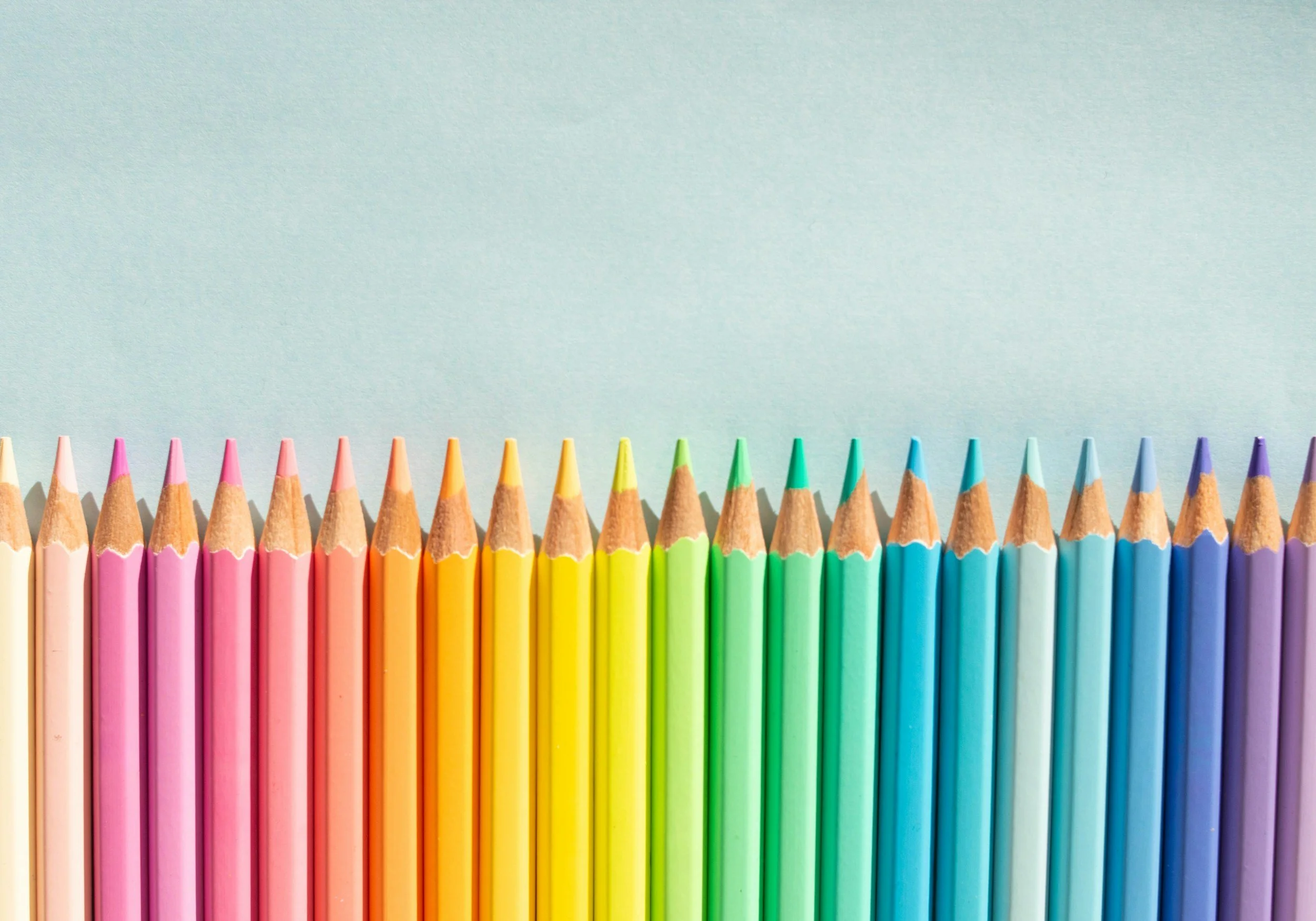 Colored pencils arranged in a row on a light blue background.