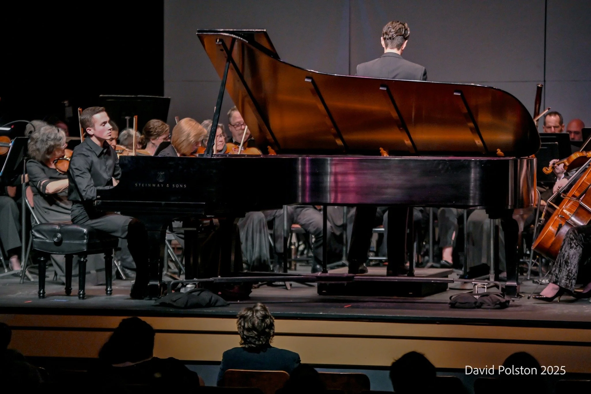 Orchestra performing on stage with a pianist in the foreground and audience members watching in the foreground.