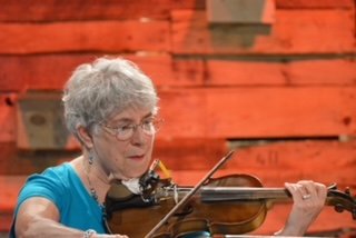 Elderly woman playing the violin in front of a red wooden wall.