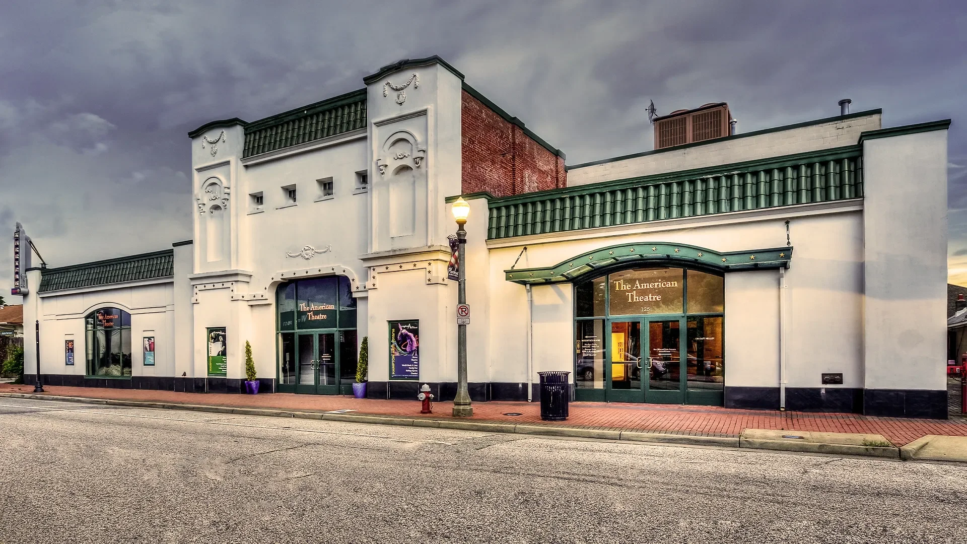 The American Theatre, a white building with green accents, large windows, and decorative features on the facade, with a sign reading 'The American Theatre' above the entrance.