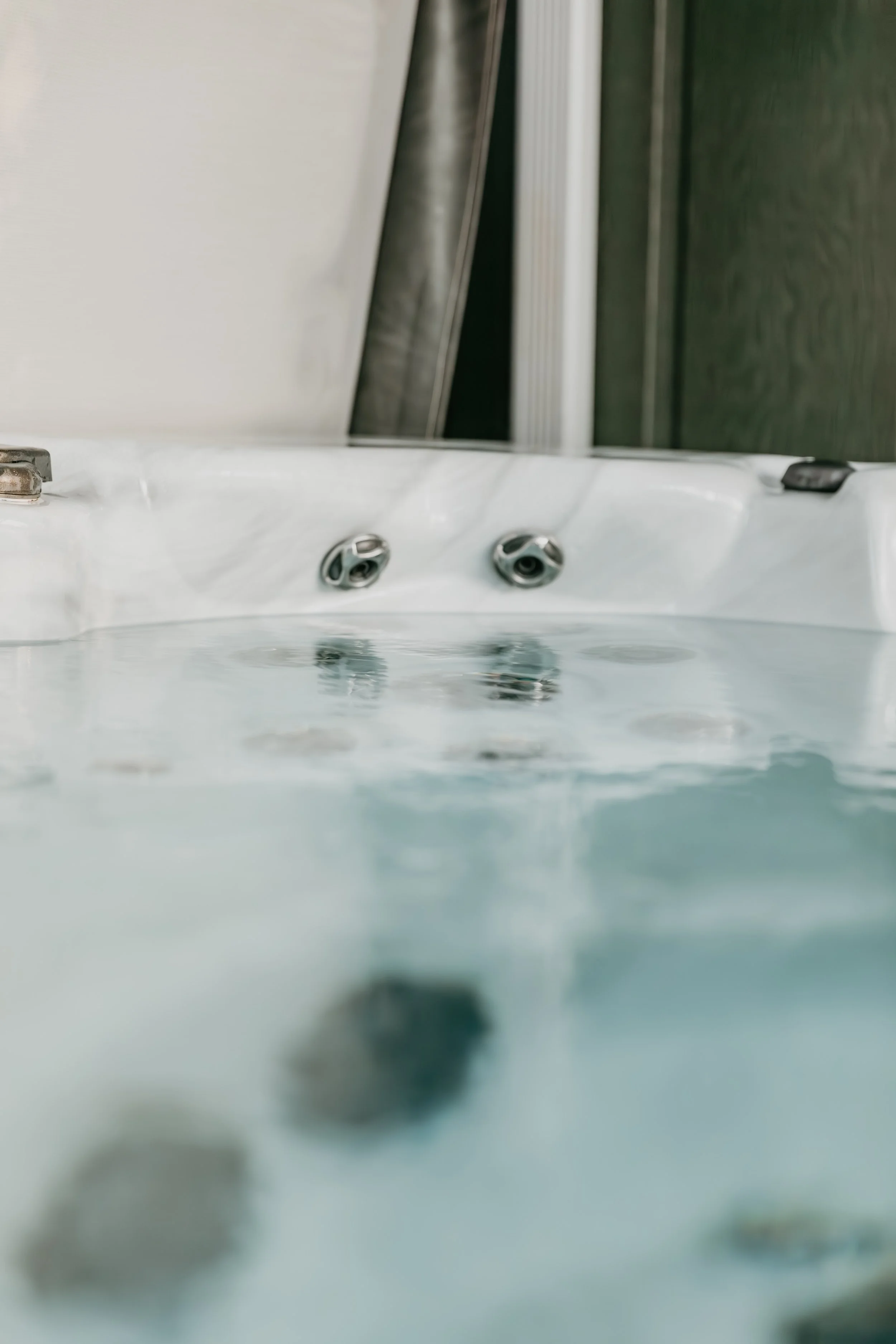 Close-up of a whirlpool hot tub with water jets and submerged rocks, with a part of a wall and spa panel in the background.