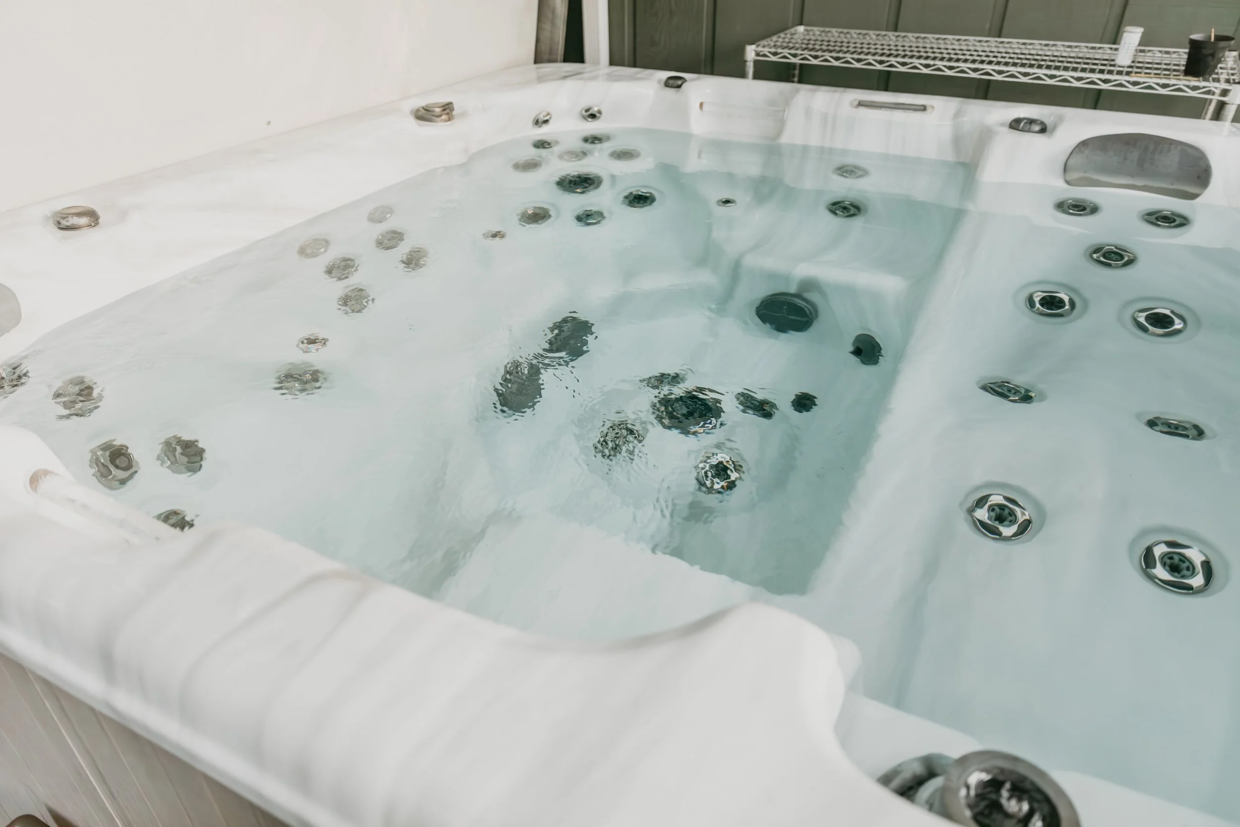 Empty white hot tub with water, multiple water jets and a metal handrail in an indoor setting.