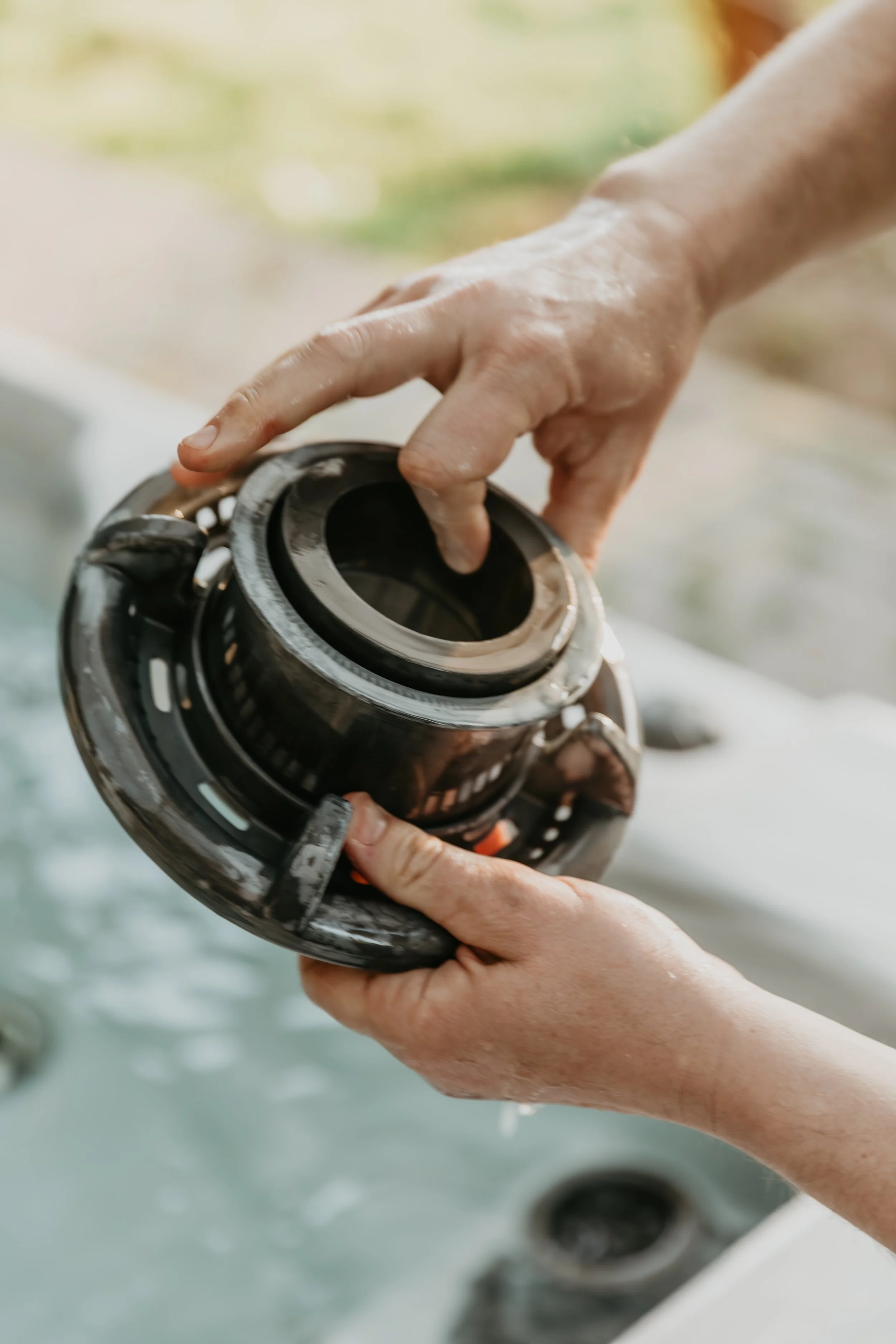 Close-up of hands holding a black jet engine turbine part over a hot tub or spa.