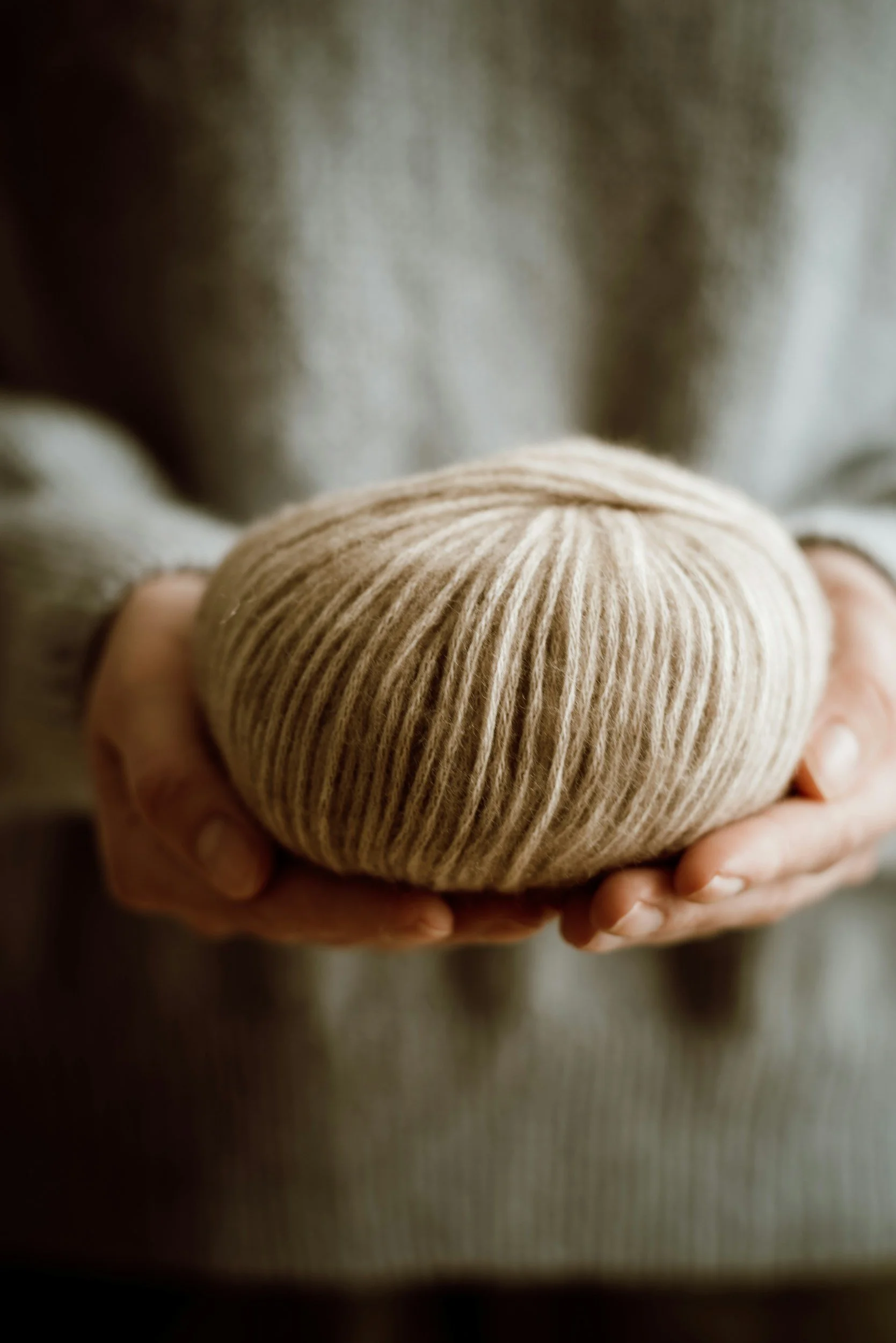 Person holding a ball of beige yarn.