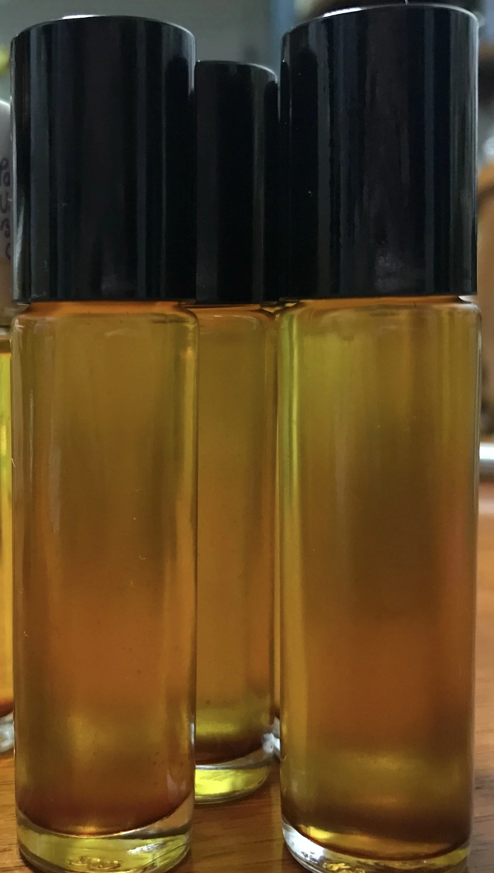 Three small bottles filled with golden liquid, with black caps, arranged closely on a wooden surface.