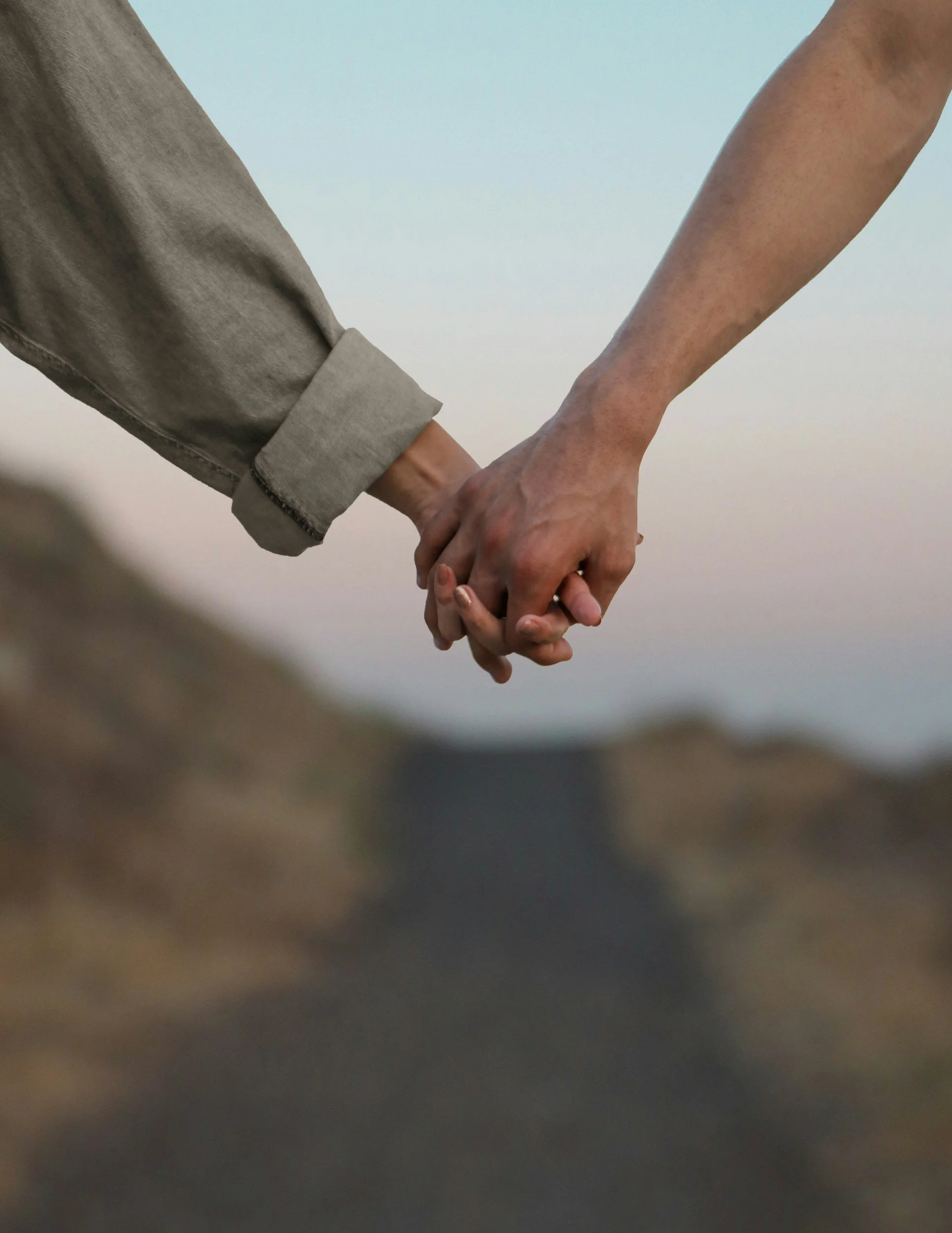 Two people holding hands, one in a gray shirt sleeve and the other in a bare arm, against a plain background.