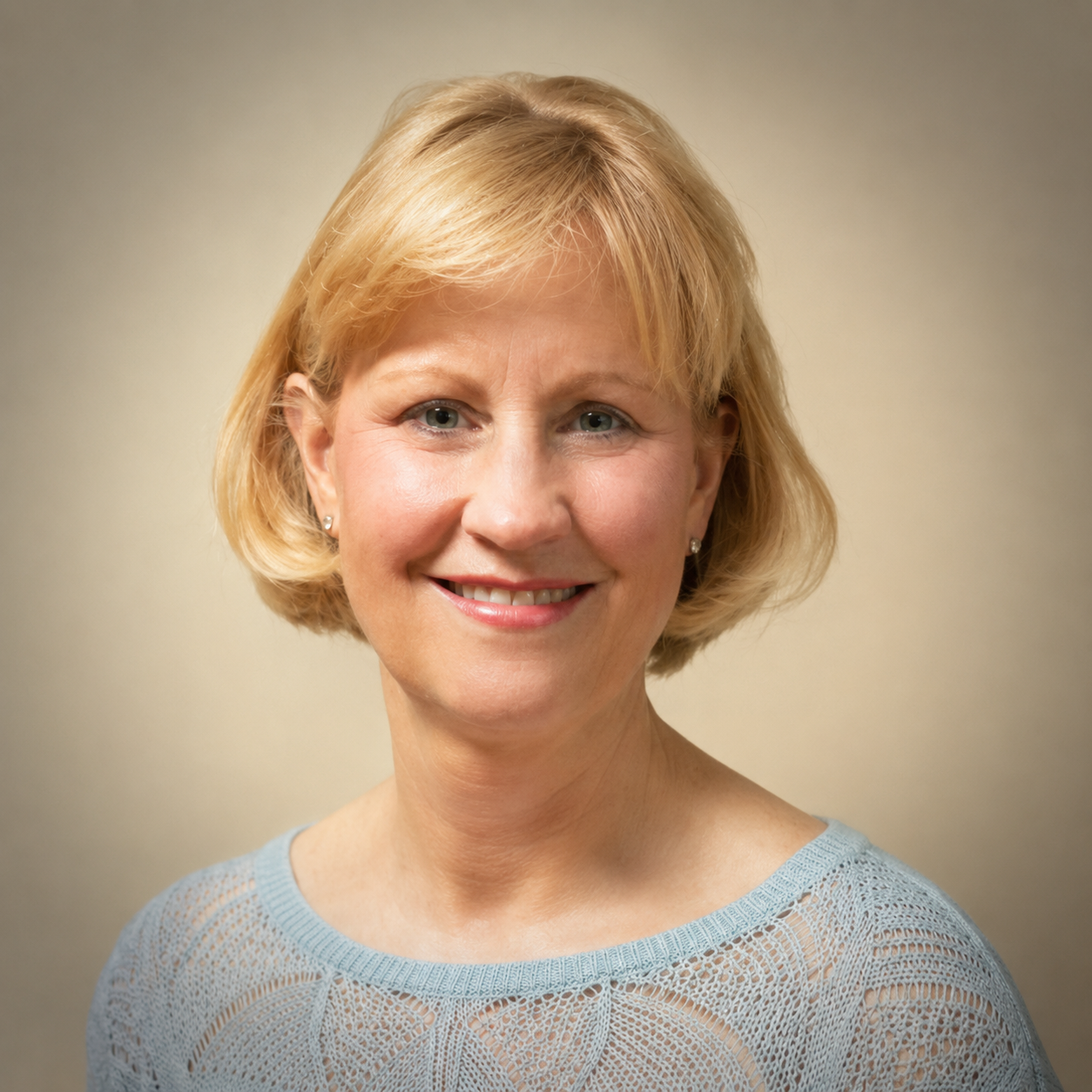 Portrait of a middle-aged woman with blonde hair, smiling, wearing a light blue sweater with lace pattern, against a plain beige background.