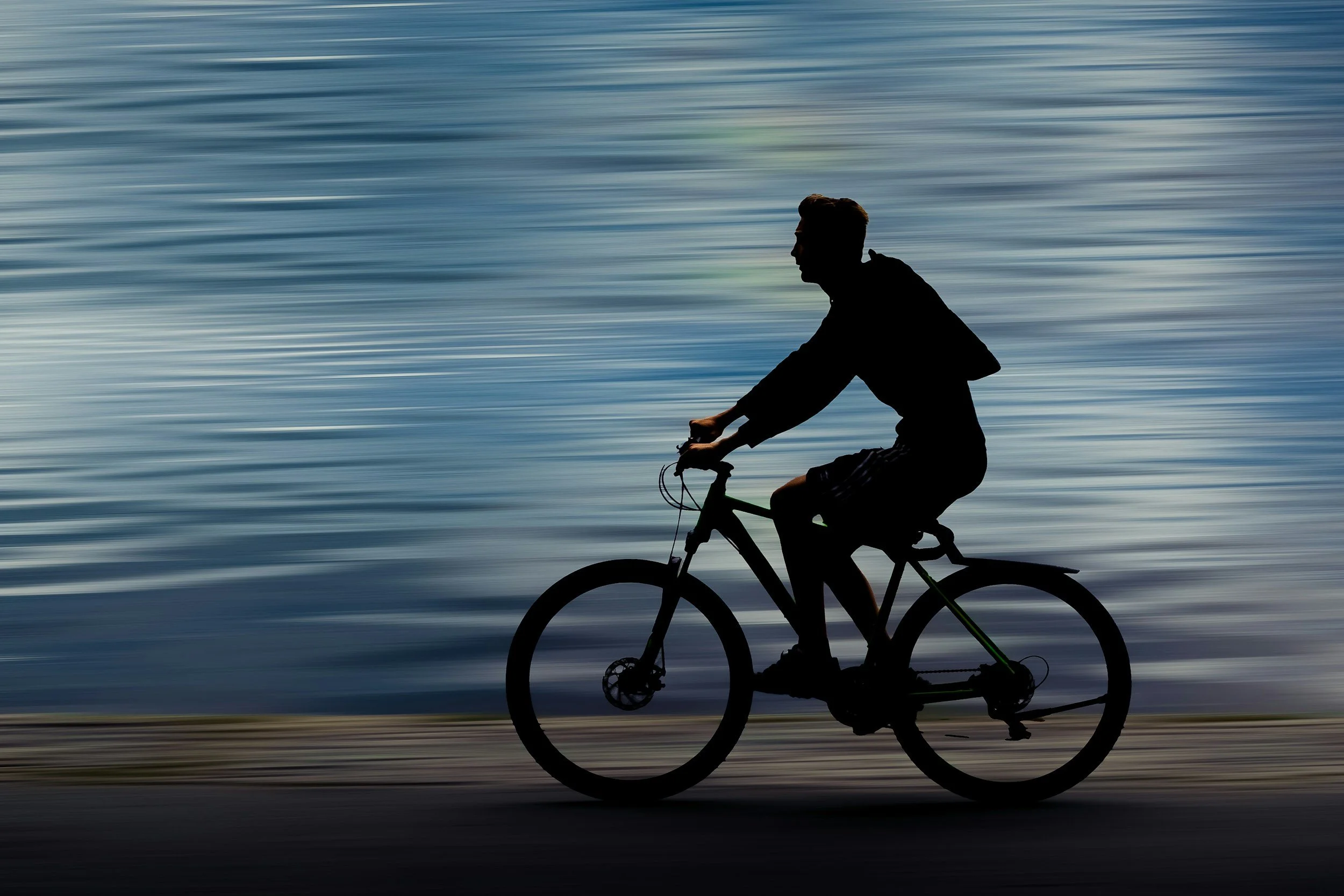 Silhouette of a person riding a bicycle along a textured water surface background.