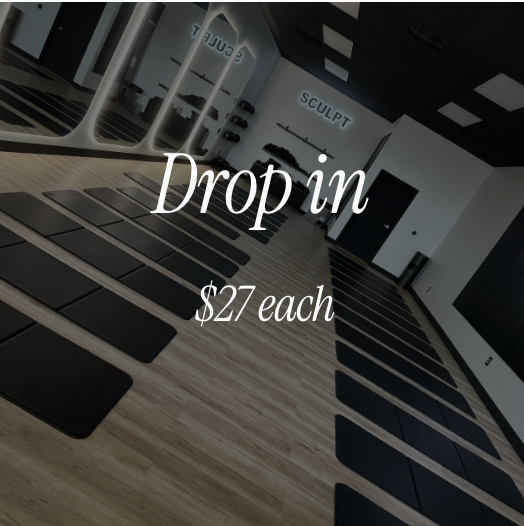 Empty fitness class studio with black mats on wooden floors, mirrors, and a wall with fitness equipment, offering drop-in classes at $27 each.