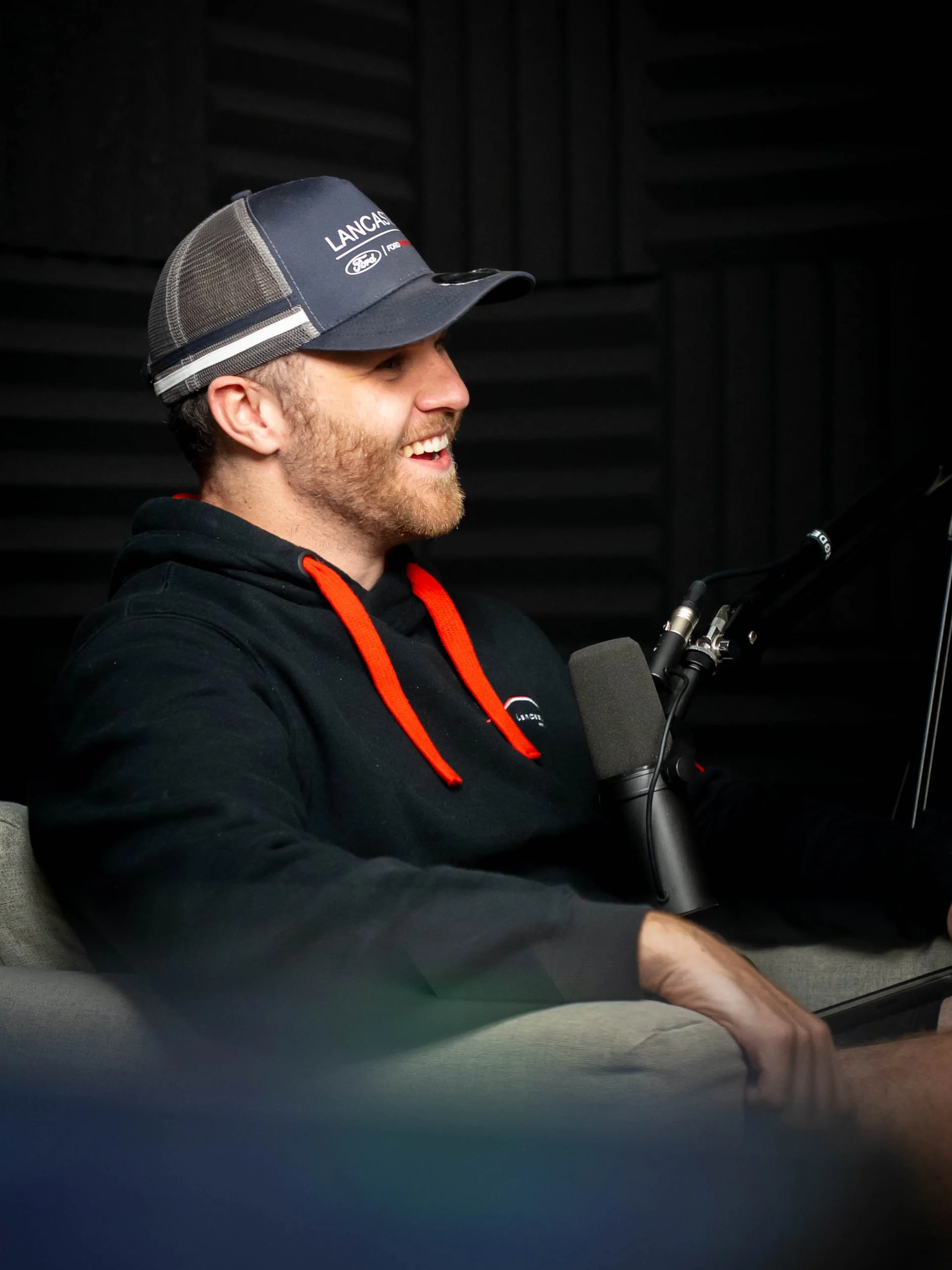 Man smiling and speaking into a microphone in a recording studio.
