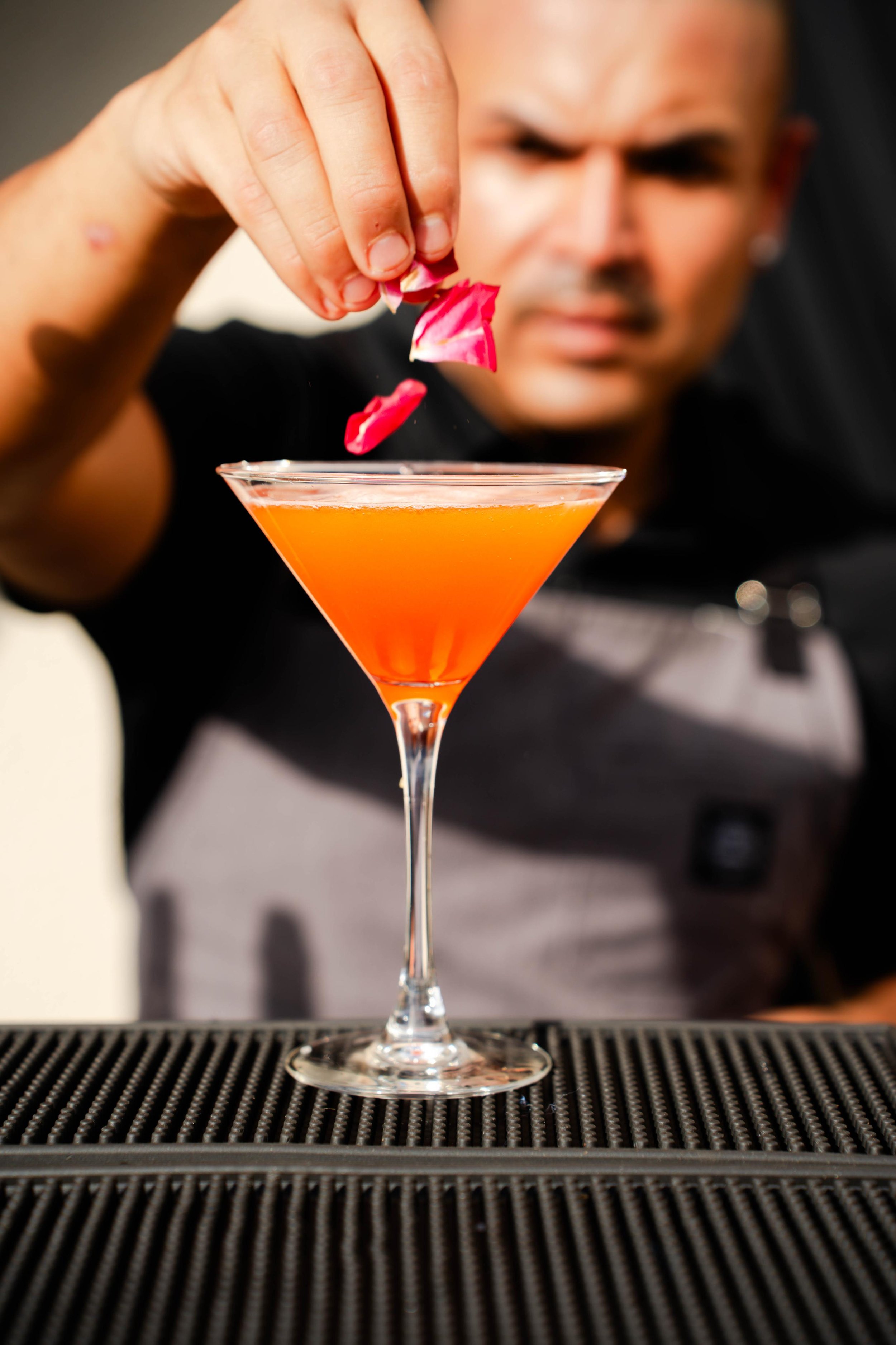 Pueblo Collective bartender garnishing a bright orange cocktail with flower petals