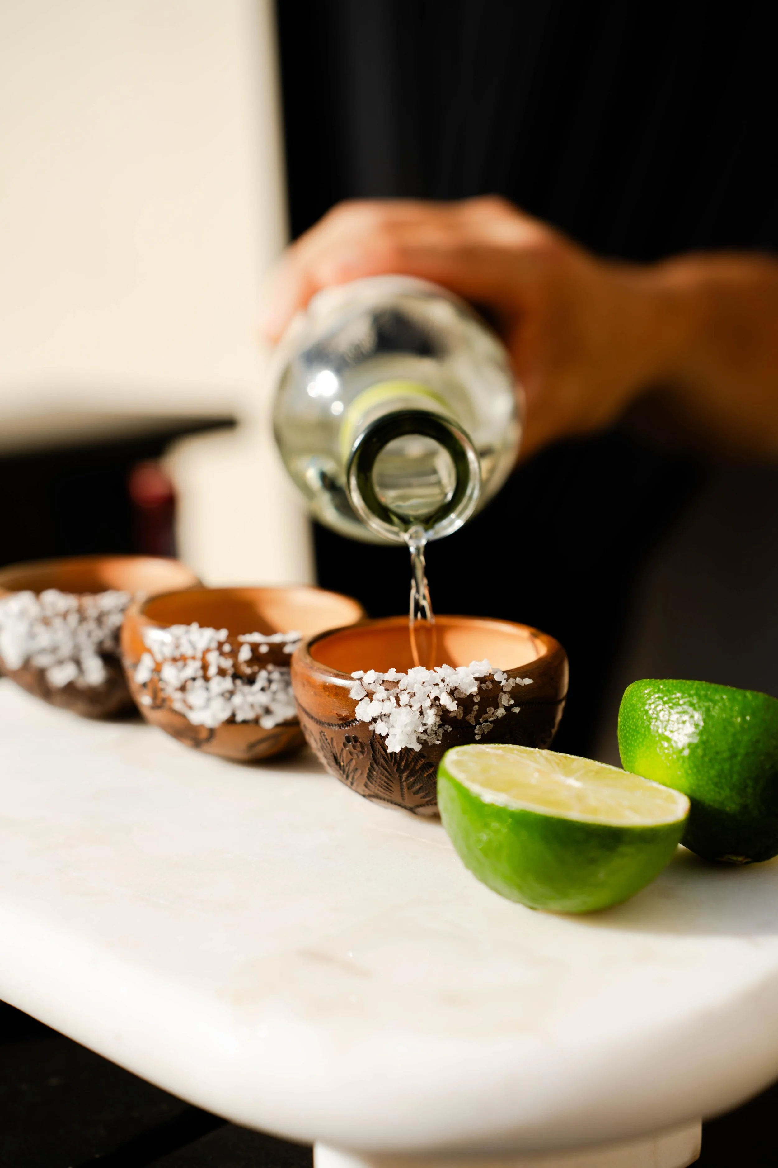Bartender pouring a drink into salt-rimmed clay cups with fresh lime