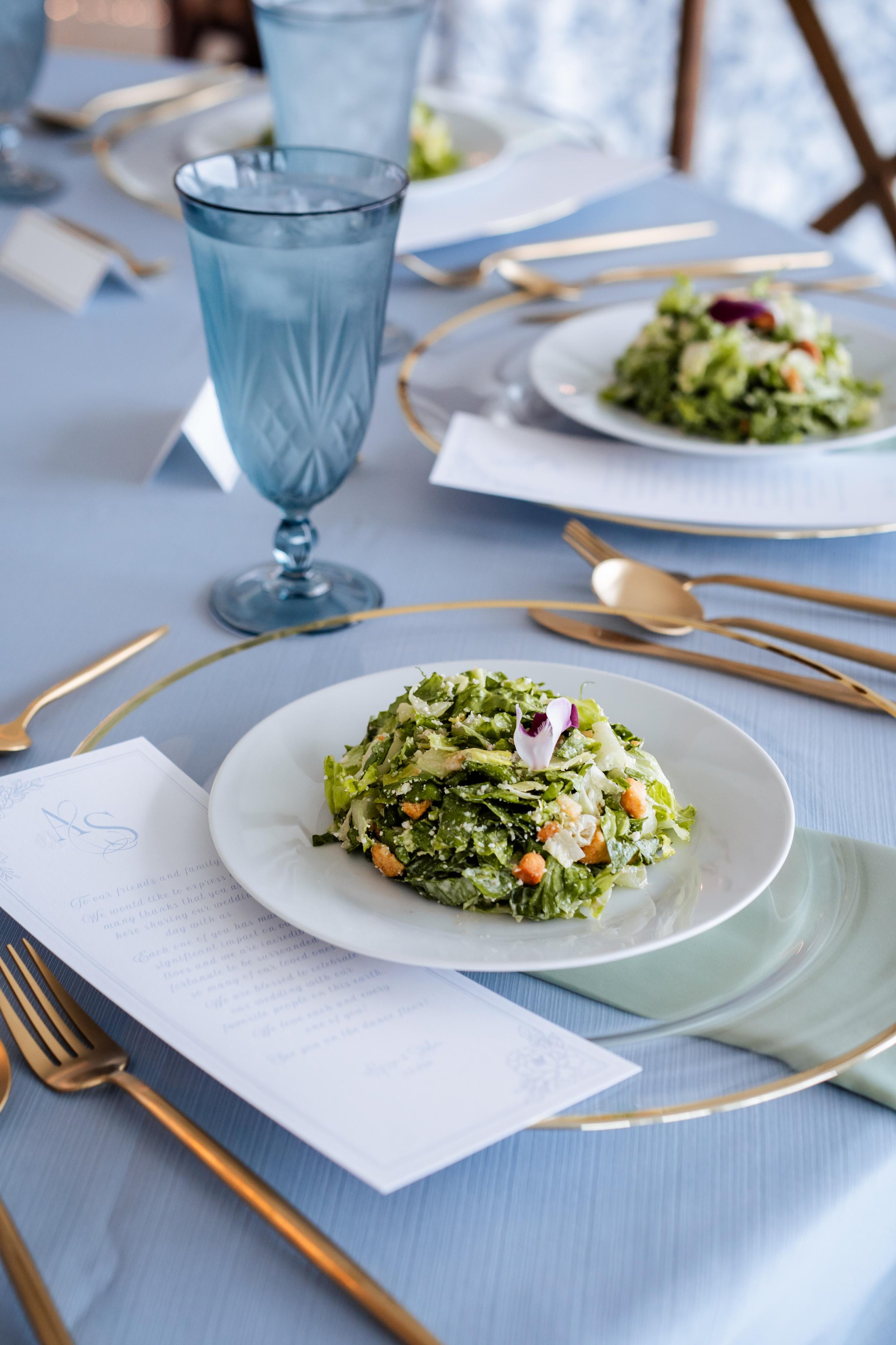 Fresh plated salads served at an elegant event table setting with blue glassware and gold flatware