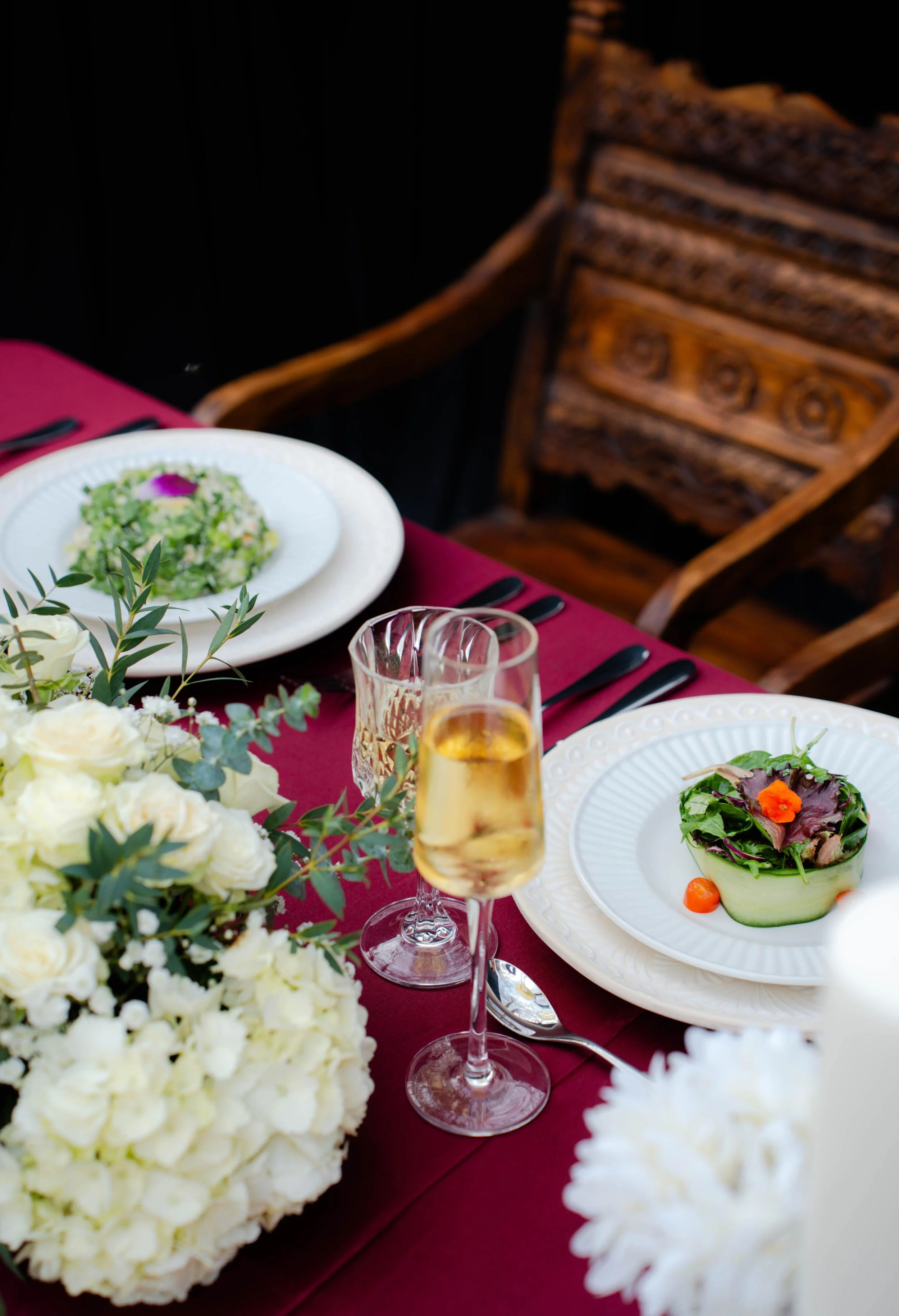 Elegant event table setting with floral arrangements, plated salads, champagne glasses, and burgundy linens
