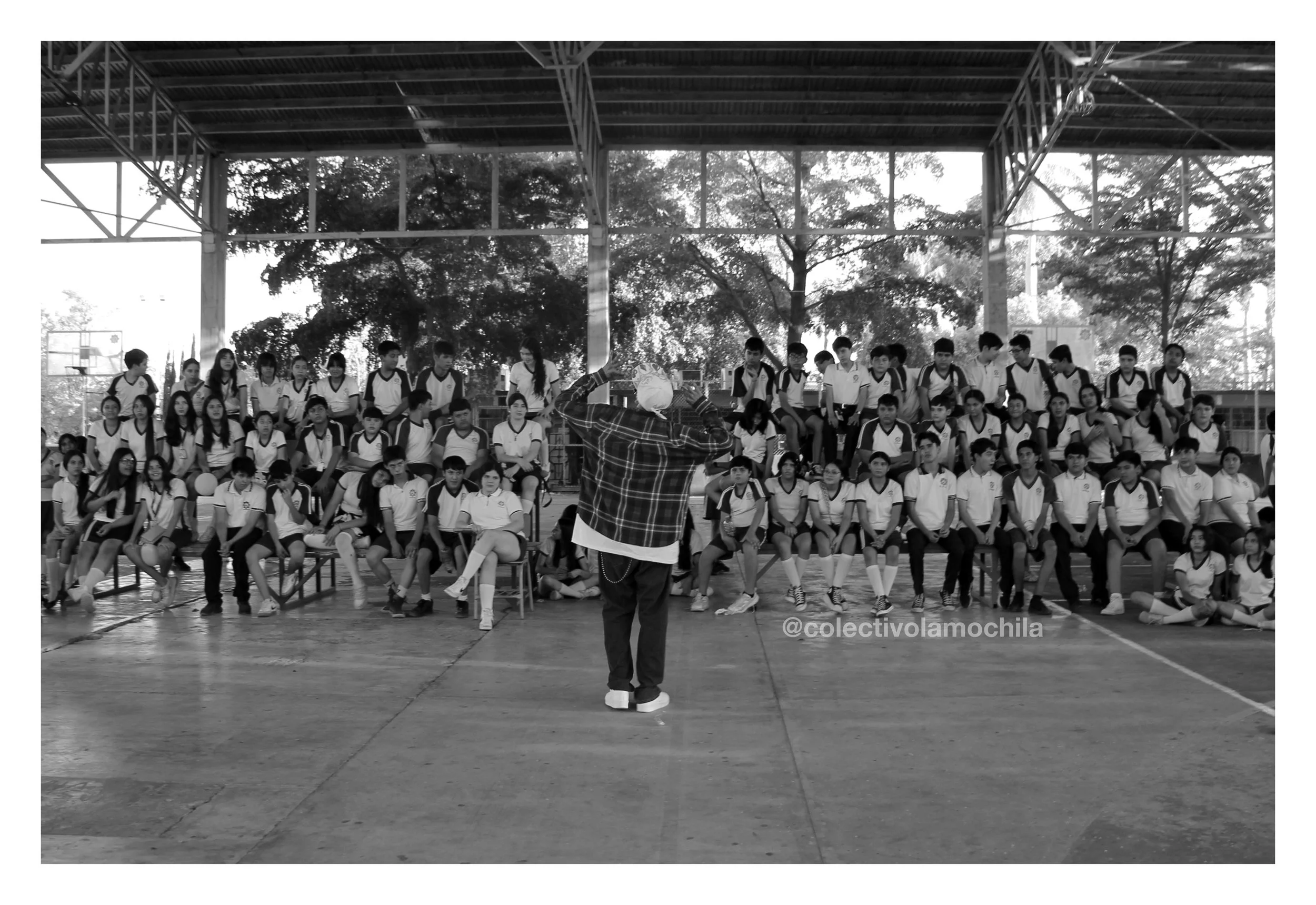 Un grupo de estudiantes vista en un auditorio en una escuela, con un cantante en el centro de la audiencia durante una presentación.