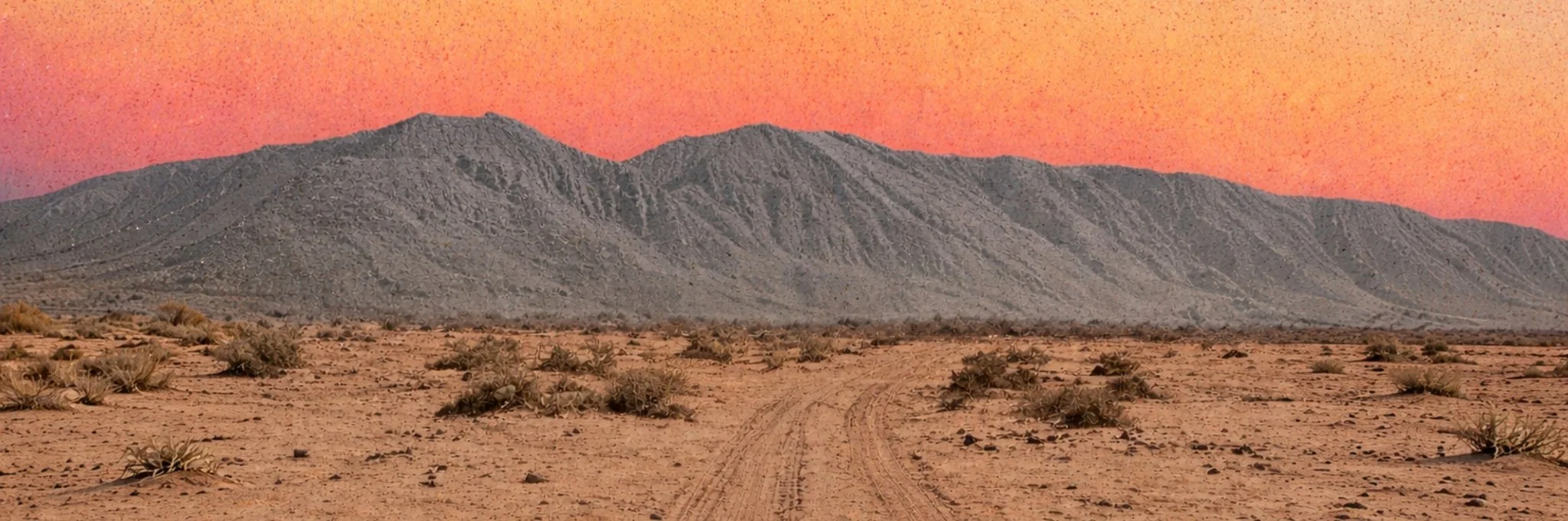 Desierto con montañas y cielo en tonos anaranjados y rosados al atardecer.