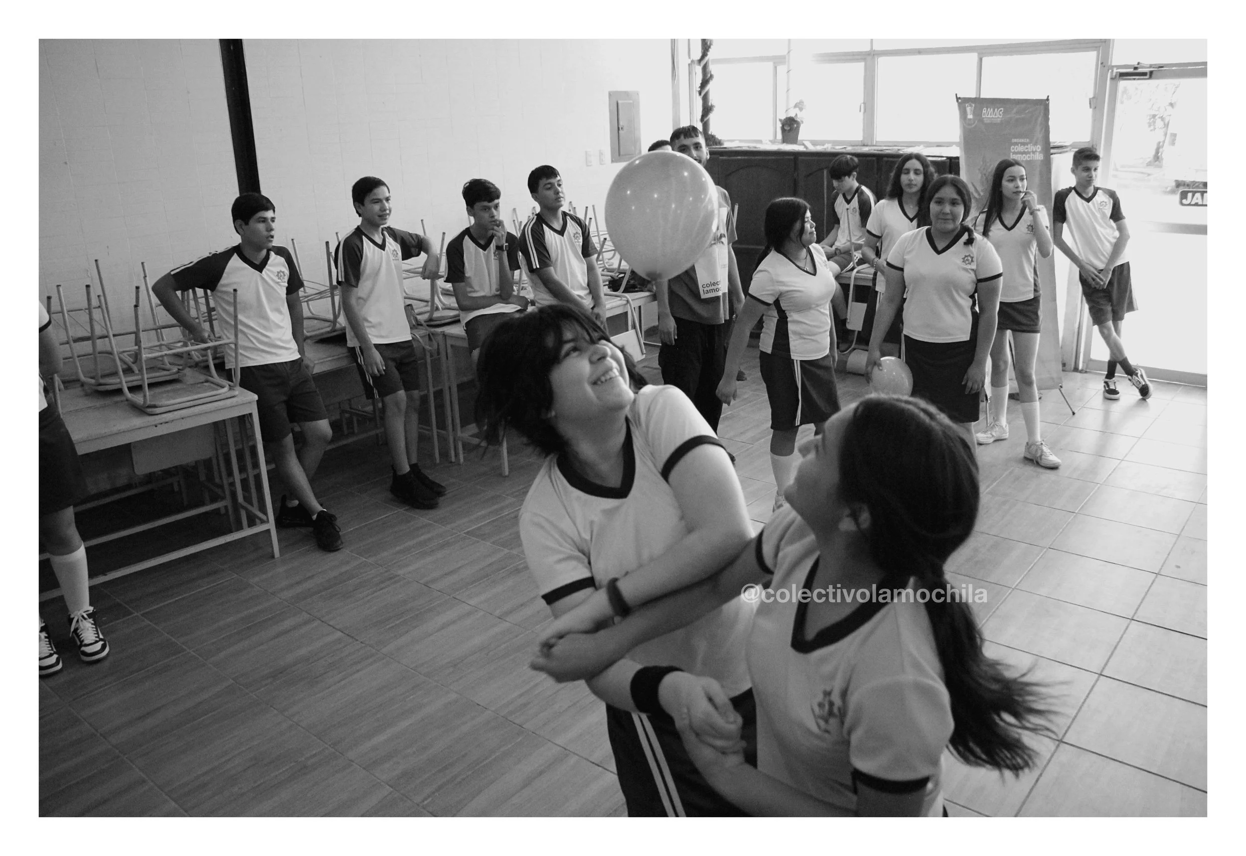 Niños en uniforme escolar jugando y divirtiéndose en una sala, algunos sosteniendo un globo, en un ambiente escolar.