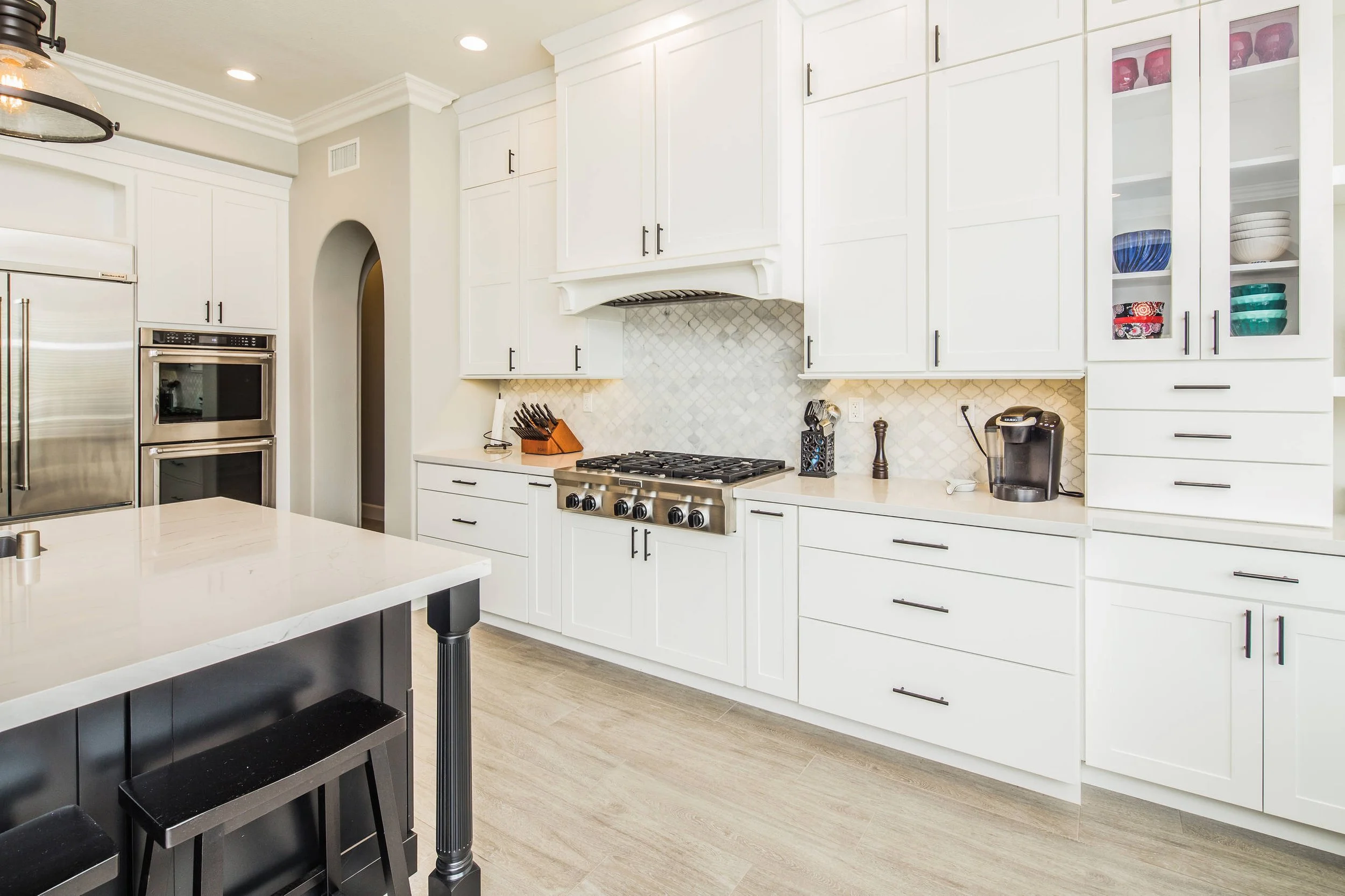 Modern kitchen with white cabinets, a stainless steel oven and microwave, a black island, and a tile backsplash.