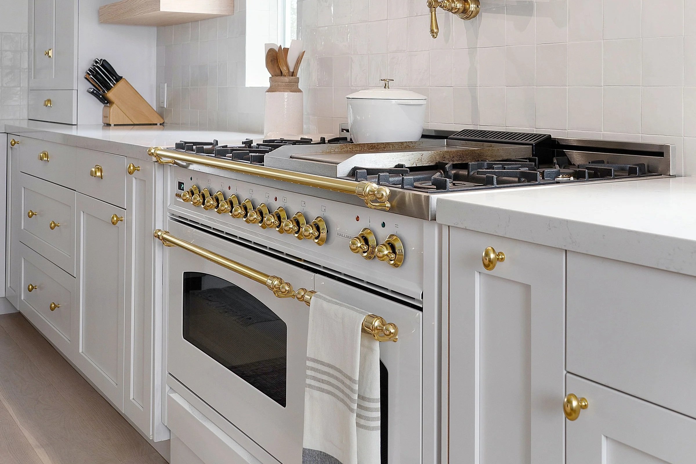 White kitchen with gold accents, stove with multiple knobs, and a white towel hanging on the oven handle.