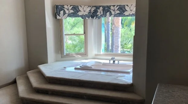 A corner of a bedroom with a built-in window seat and a view of tropical trees outside.