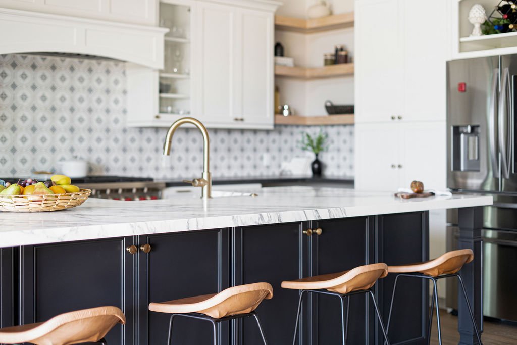 Modern kitchen with white upper cabinets, black lower cabinets, a marble countertop, a gold faucet, a basket of fruit, and open shelving.