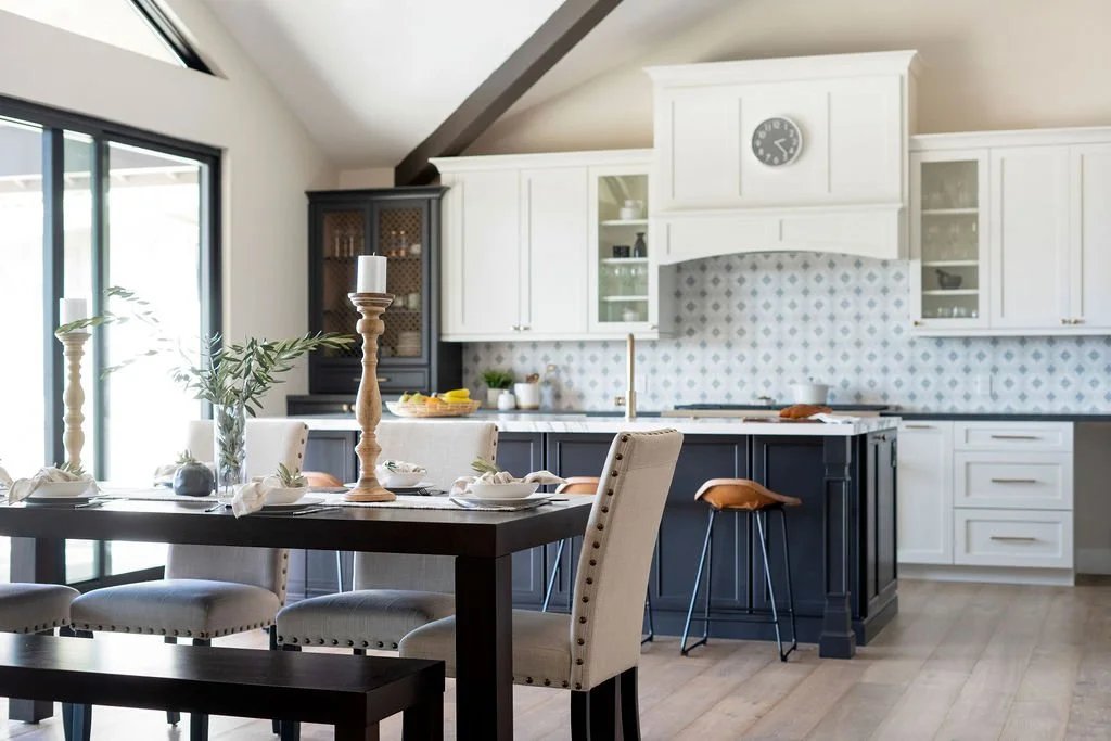 Modern kitchen and dining area with white cabinets, a black kitchen island, a dining table with chairs, and large windows letting in natural light.