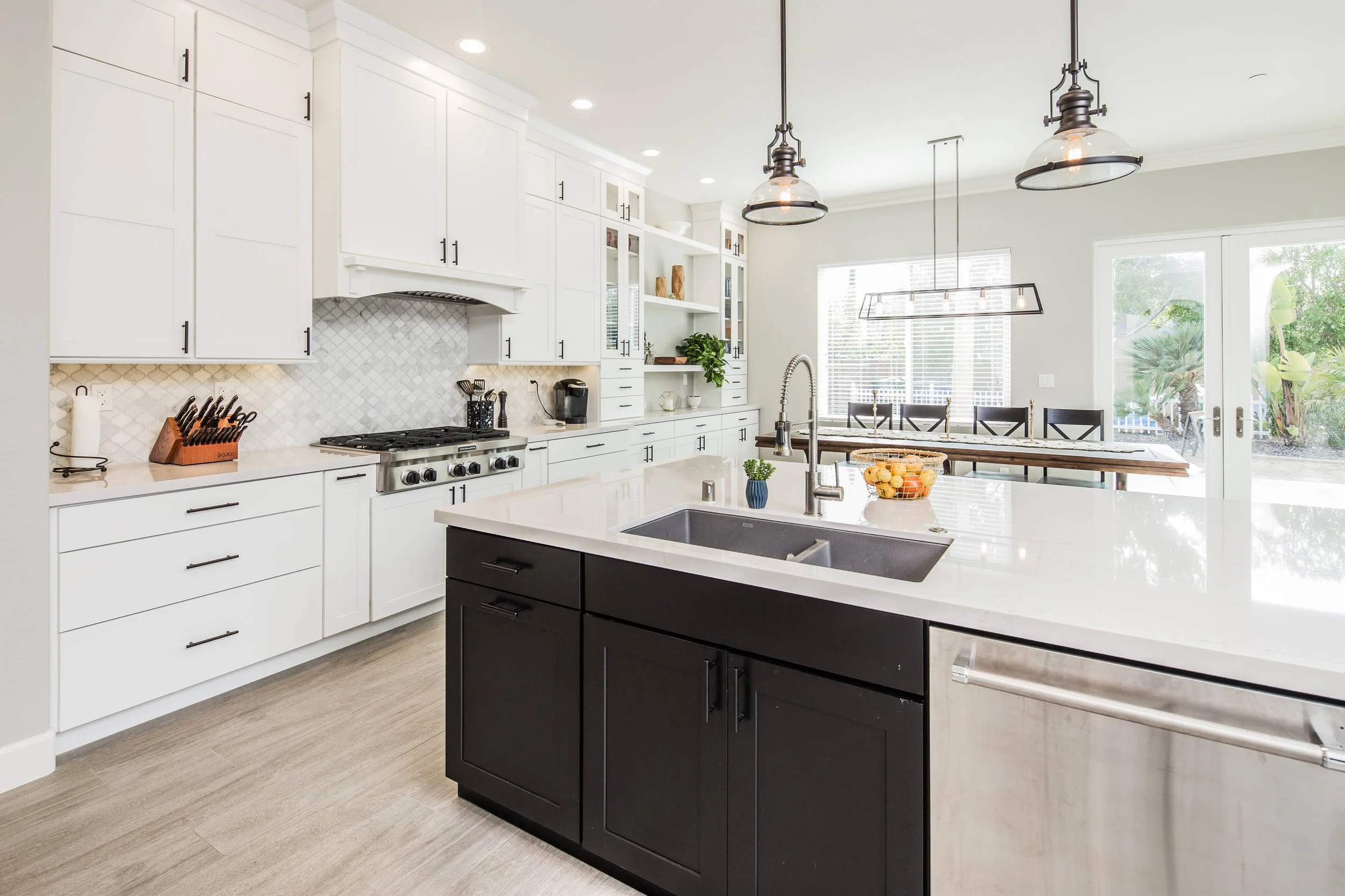 Modern kitchen with white cabinets, a black kitchen island, stainless steel appliances, and large windows with outdoor greenery.