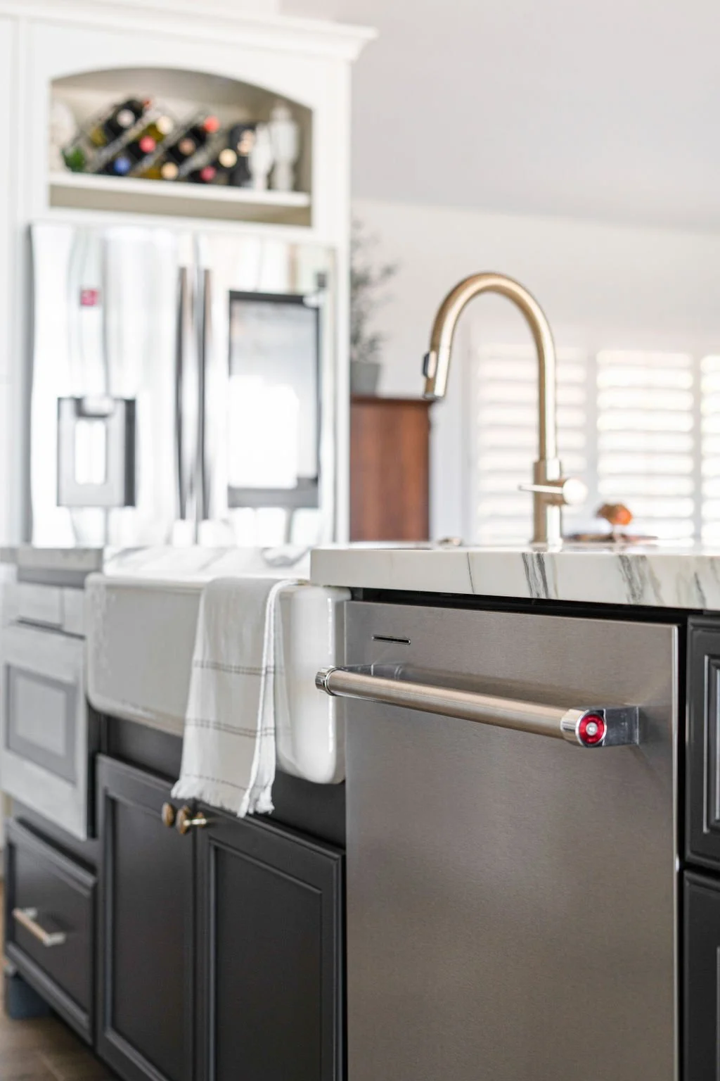Modern kitchen with black cabinets, stainless steel appliances, marble countertop, and brass faucet, with a dish towel hanging over the dishwasher.