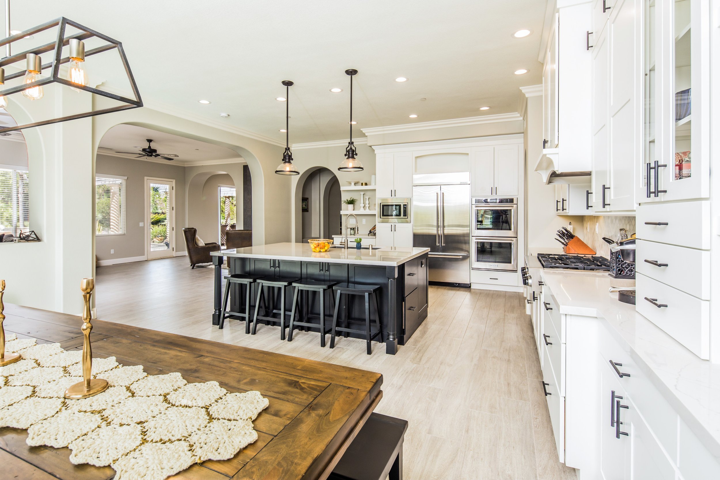 Modern kitchen with white cabinets, stainless steel appliances, island with seating, pendant lighting, and open dining area with windows and sliding door.