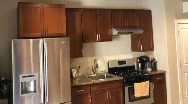 Kitchen with stainless steel French door refrigerator, brown wooden cabinets, black stove, and small appliances on countertops.