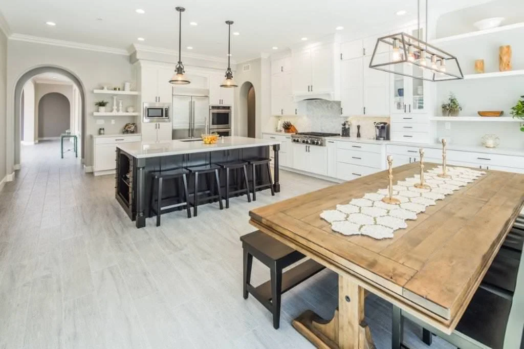 Modern kitchen with white cabinets, a large island with a black base, and a wooden dining table with a white table runner and candlesticks.