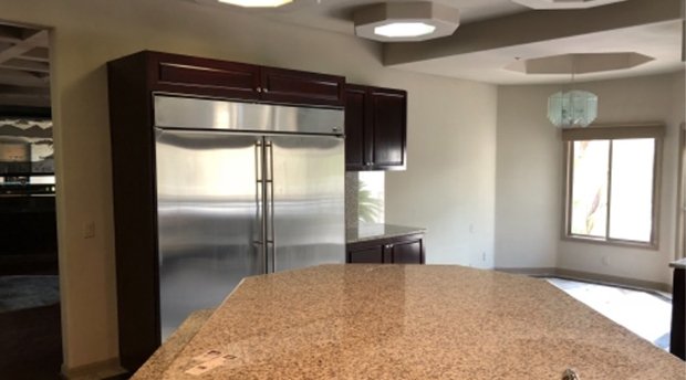 View of a kitchen with a granite countertop island, stainless steel refrigerator, dark wooden cabinets, a window, and a ceiling light fixture.