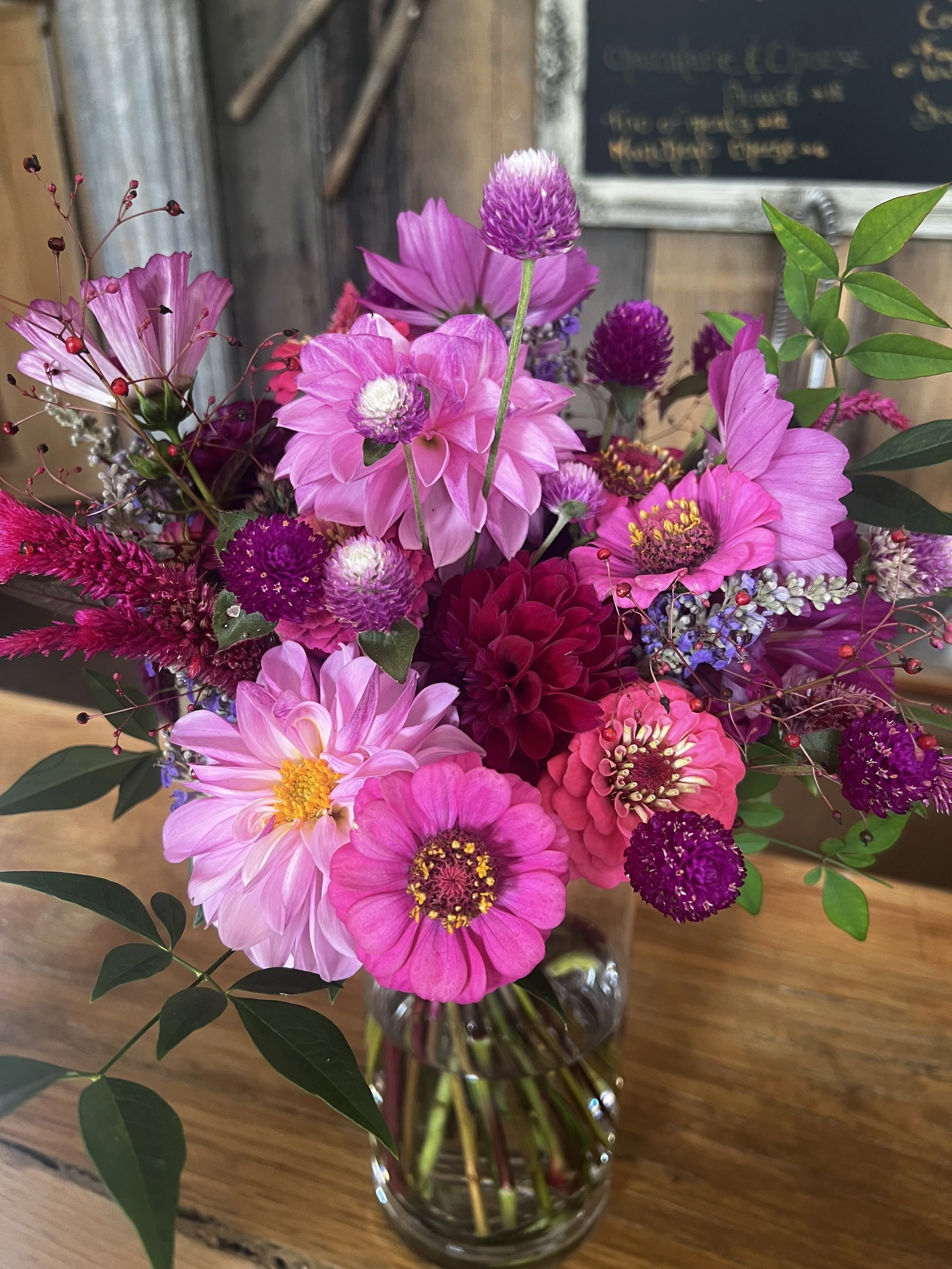 A colorful bouquet of pink, purple, and magenta flowers in a glass vase on a wooden table.